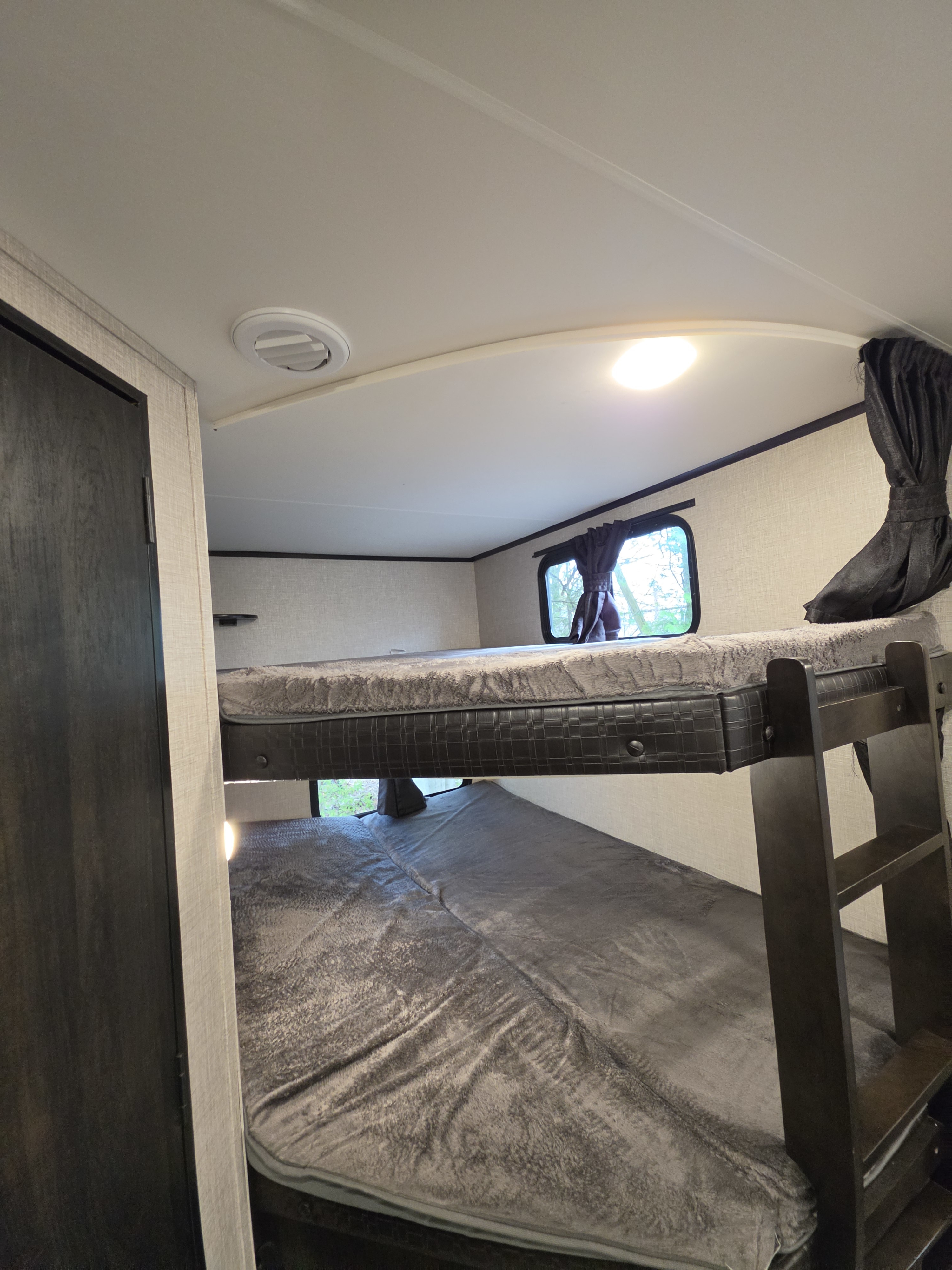 Spacious RV rental bunk beds with cozy grey blankets, a window view, and ceiling light, ready for your next adventure.. Jayco Jay Feather 2021