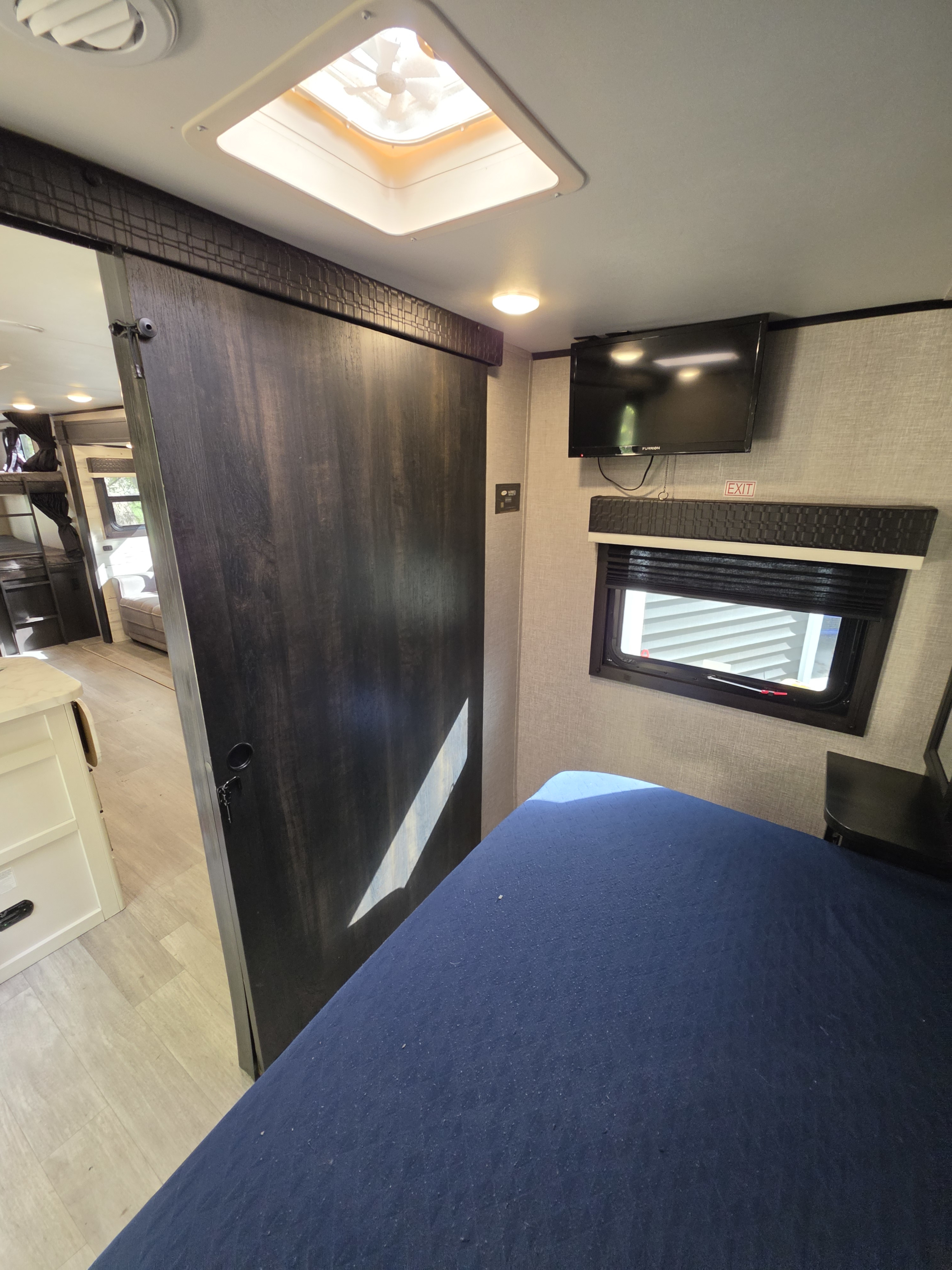 Cozy rv rental interior showing a bedroom with a blue bed, sliding door to bunk beds, TV, and window.. Jayco Jay Feather 2021