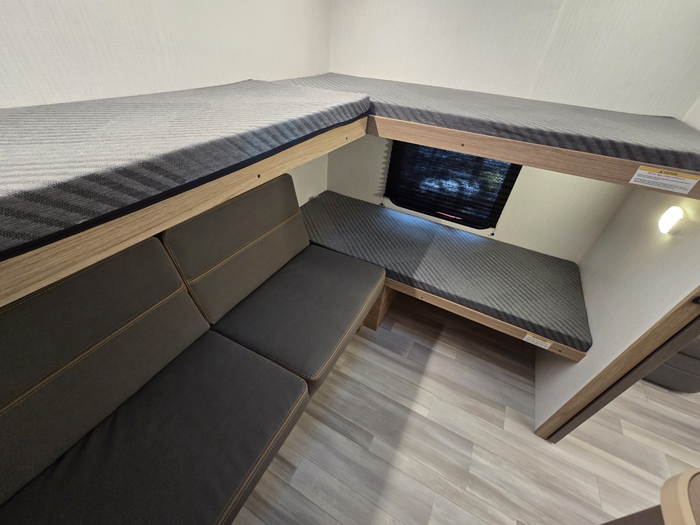 Cozy rv rental interior: L-shaped bunk beds & a lower sleeping area with a couch/dinette, all with striped cushions. Perfect for travel.. Cruiser RV Avenir 2025
