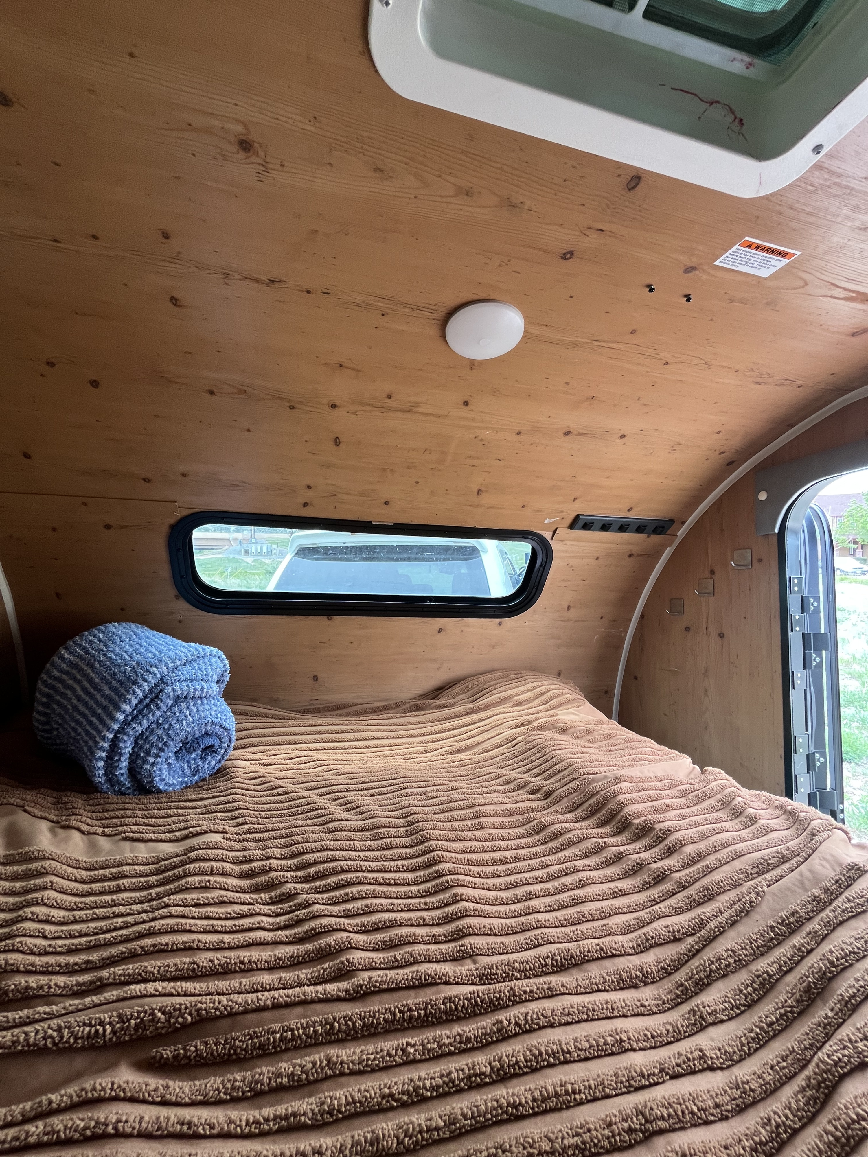 Cozy RV rental interior with wood walls, comfy bed, and blue blanket. Perfect for travel adventures and comfortable nights.. Sunset Park RV SunRay 2021