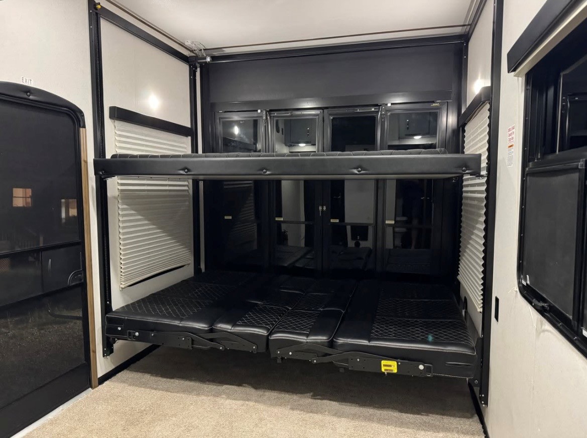 Inside an rv rental, a versatile toy hauler garage with a two-tier black bunk bed system, lower section configured as a sofa-bed.. Keystone Fuzion 2020