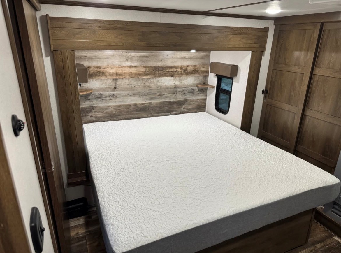 Comfortable RV rental bedroom featuring a large bed, rustic wood headboard, window, and wardrobes, perfect for travel.. Keystone Fuzion 2020
