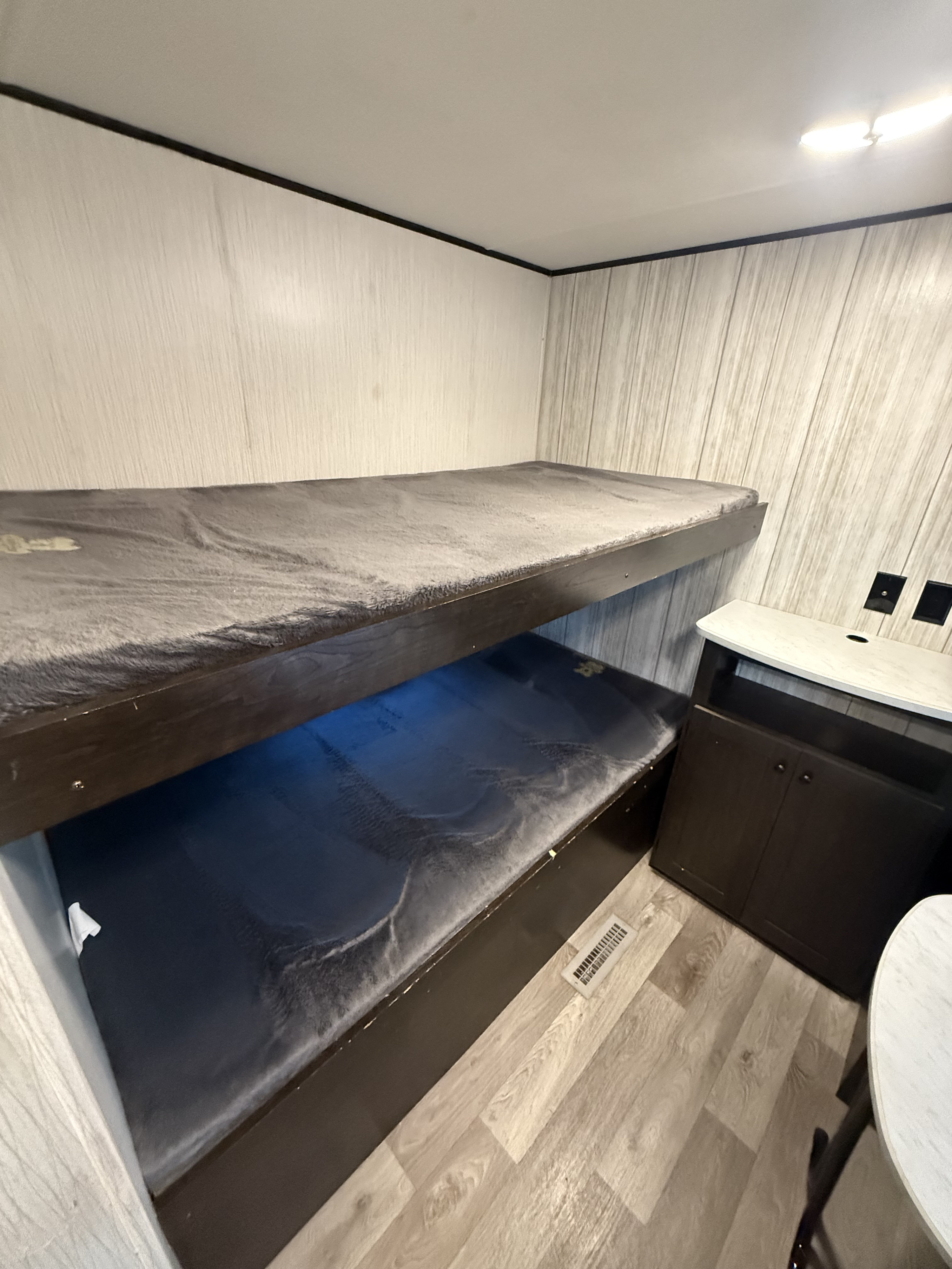 Inside an RV rental, showing compact bunk beds with gray bedding and a small storage cabinet, maximizing space for travelers.. Pioneer QB300 2021