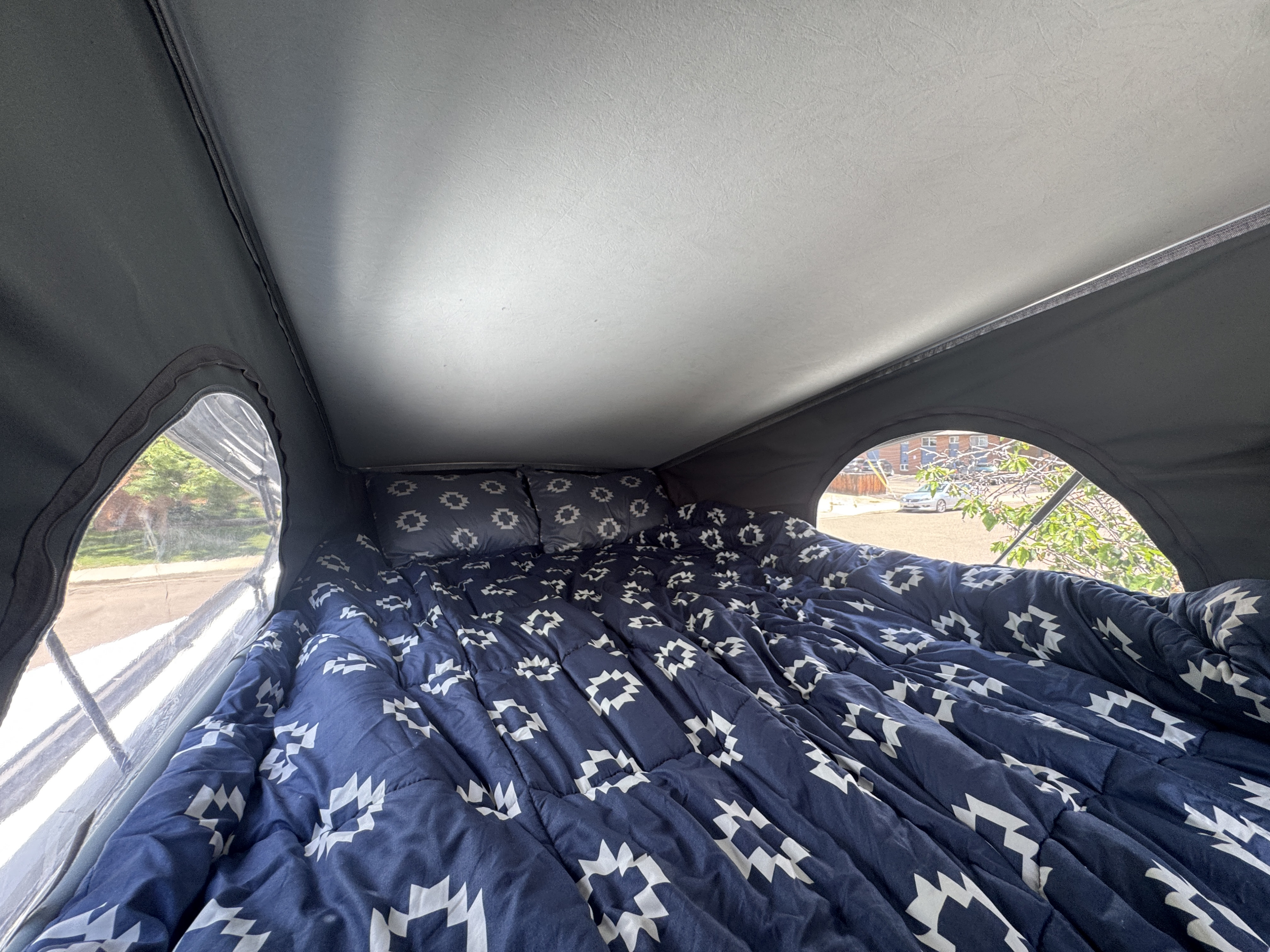 Cozy RV rental pop-top sleeping area with a blue patterned comforter and pillows, offering outdoor views.. Winnebago Ekko 2022