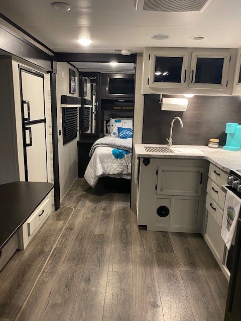 Modern RV rental interior featuring a galley kitchen, cozy bedroom, and wood-look flooring for travel comfort.. Jayco 24BH 2021