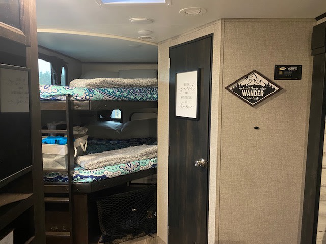 This RV rental interior features cozy bunk beds with patterned bedding, a door, and wall decor. Ideal for family trips.. Jayco 24BH 2021