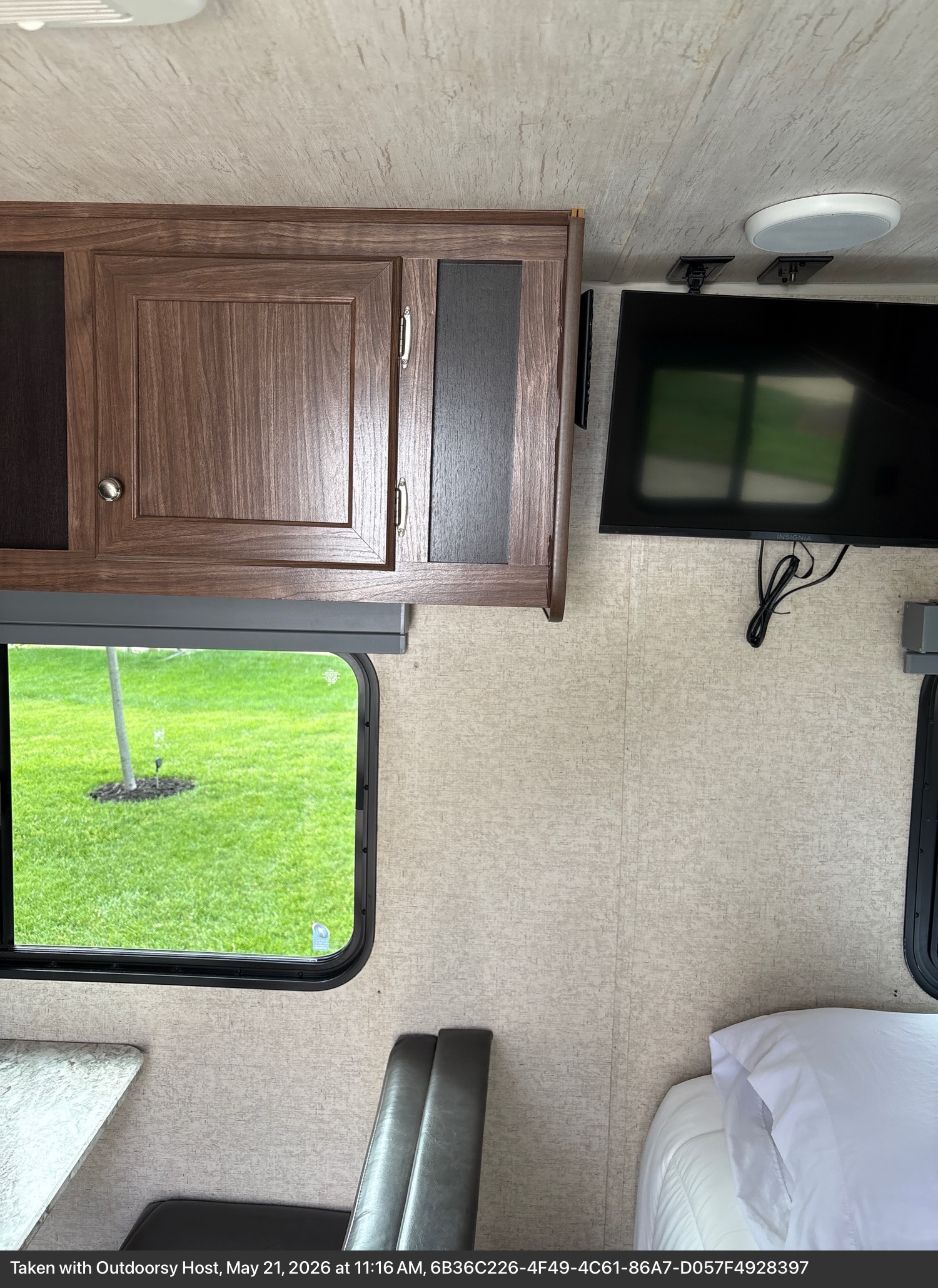 RV rental interior with wood cabinets, wall-mounted TV, window view of green grass, dinette seat, and bed.. Heartland RVs Pioneer 2018
