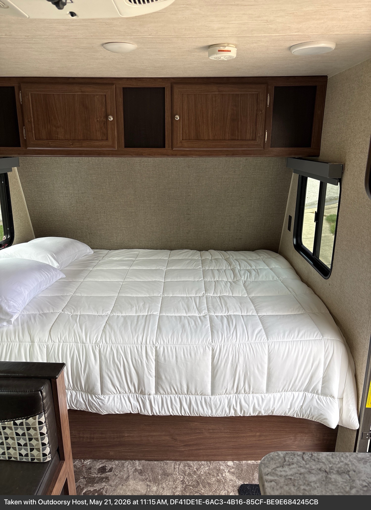 This RV rental features a comfortable queen bed with white comforter and pillows, overhead cabinets, and side windows for a cozy bedroom.. Heartland RVs Pioneer 2018