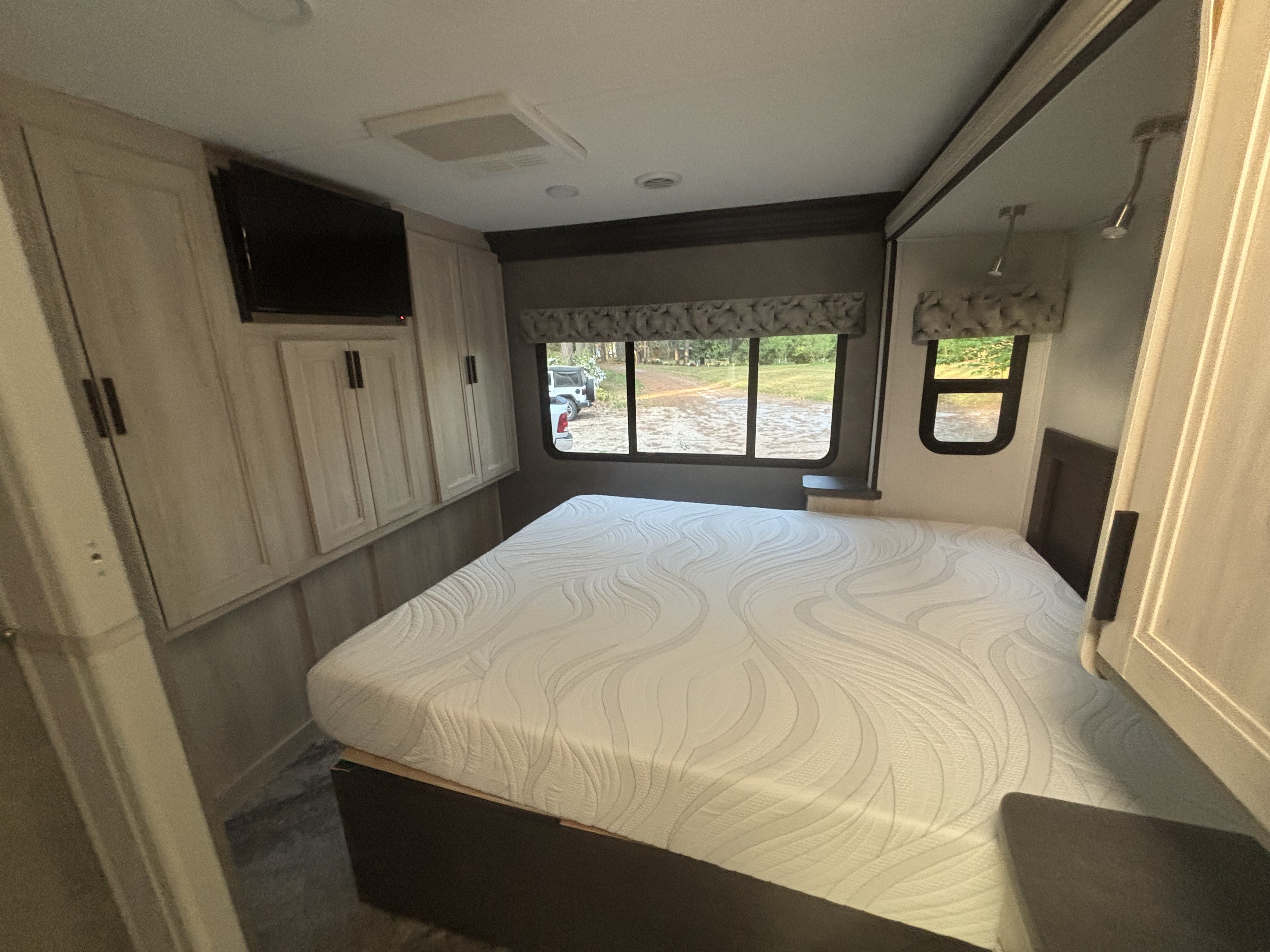 Cozy RV rental bedroom showing a bed, light wood cabinets, TV, and large windows with outdoor views, perfect for your next adventure.. Forest River Sunseeker 2020