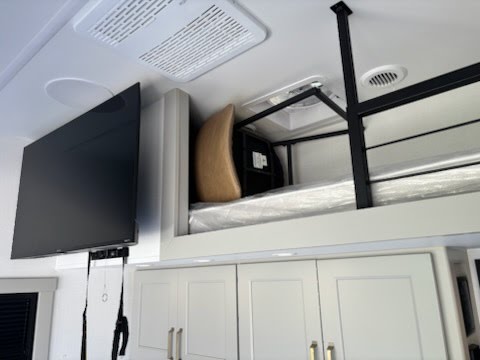 Inside this modern RV rental, a mounted TV and high bunk bed with a new mattress in plastic are above storage cabinets.. Brinkley RV Model G Toy Hauler 2025