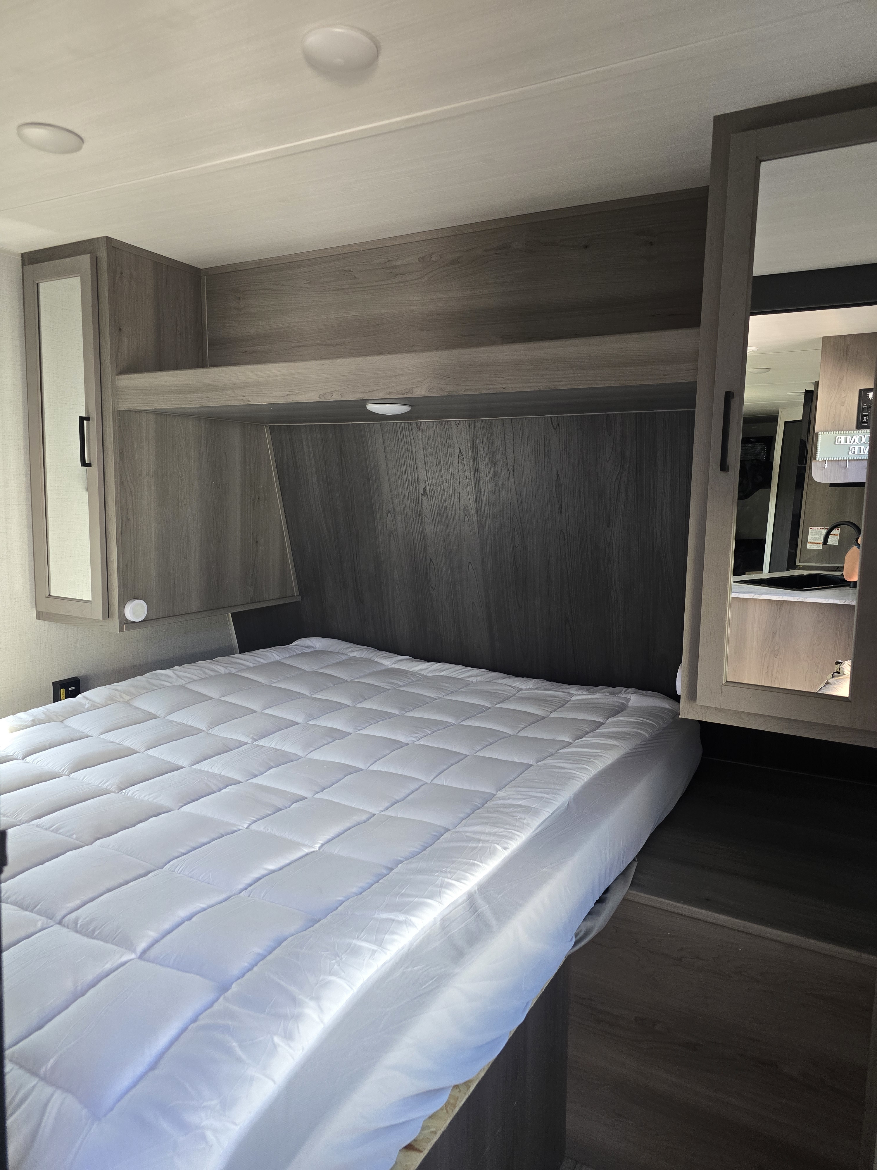 Modern RV rental bedroom featuring a comfy bed with a quilted topper, ample overhead storage, and sleek wood-look finishes.. Keystone RV Hideout 2024