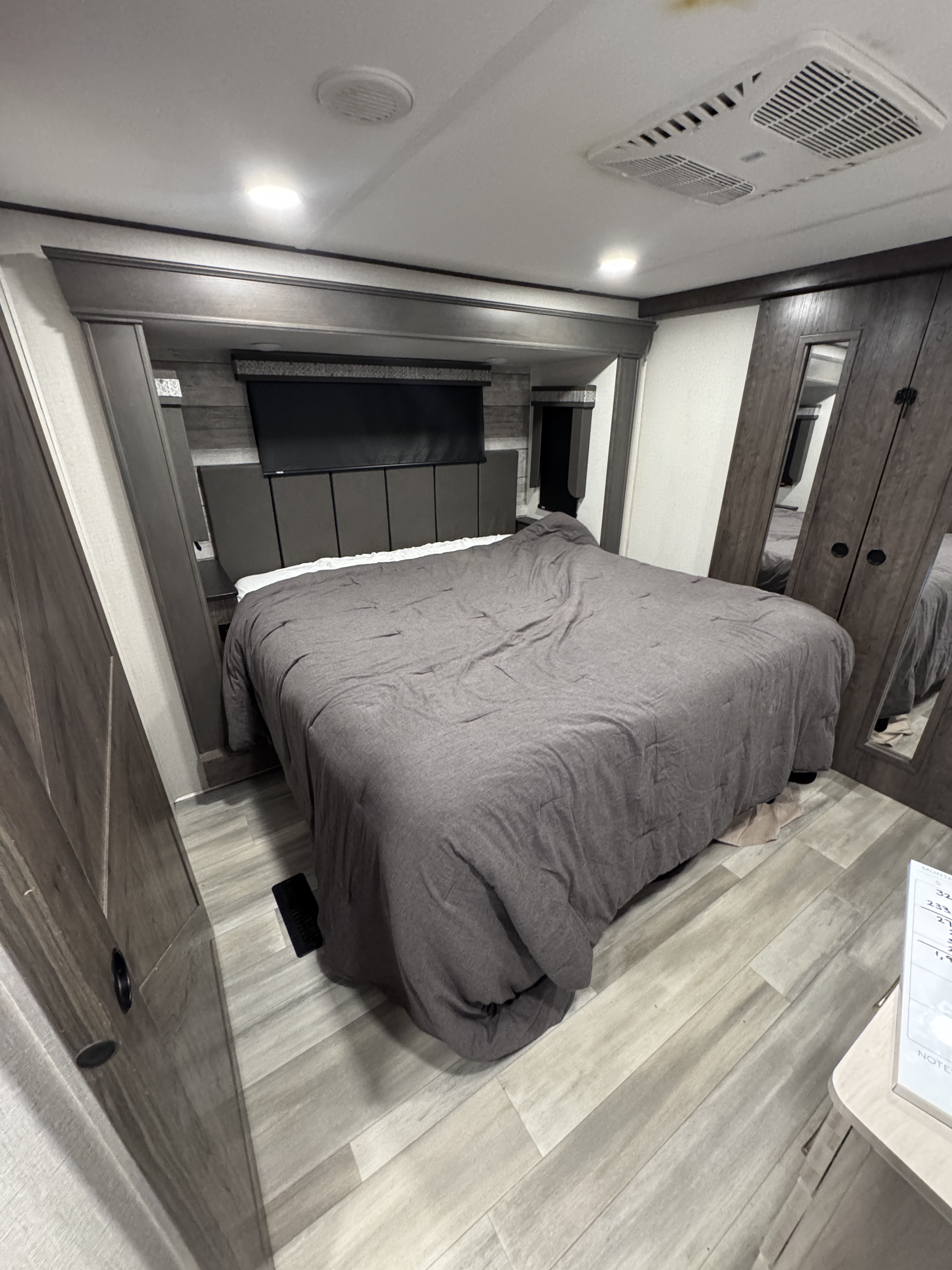 Cozy RV rental bedroom with a grey bed, headboard, wall-mounted TV, and ceiling AC unit, featuring wood-look flooring.. Alliance RV Paradigm 2021
