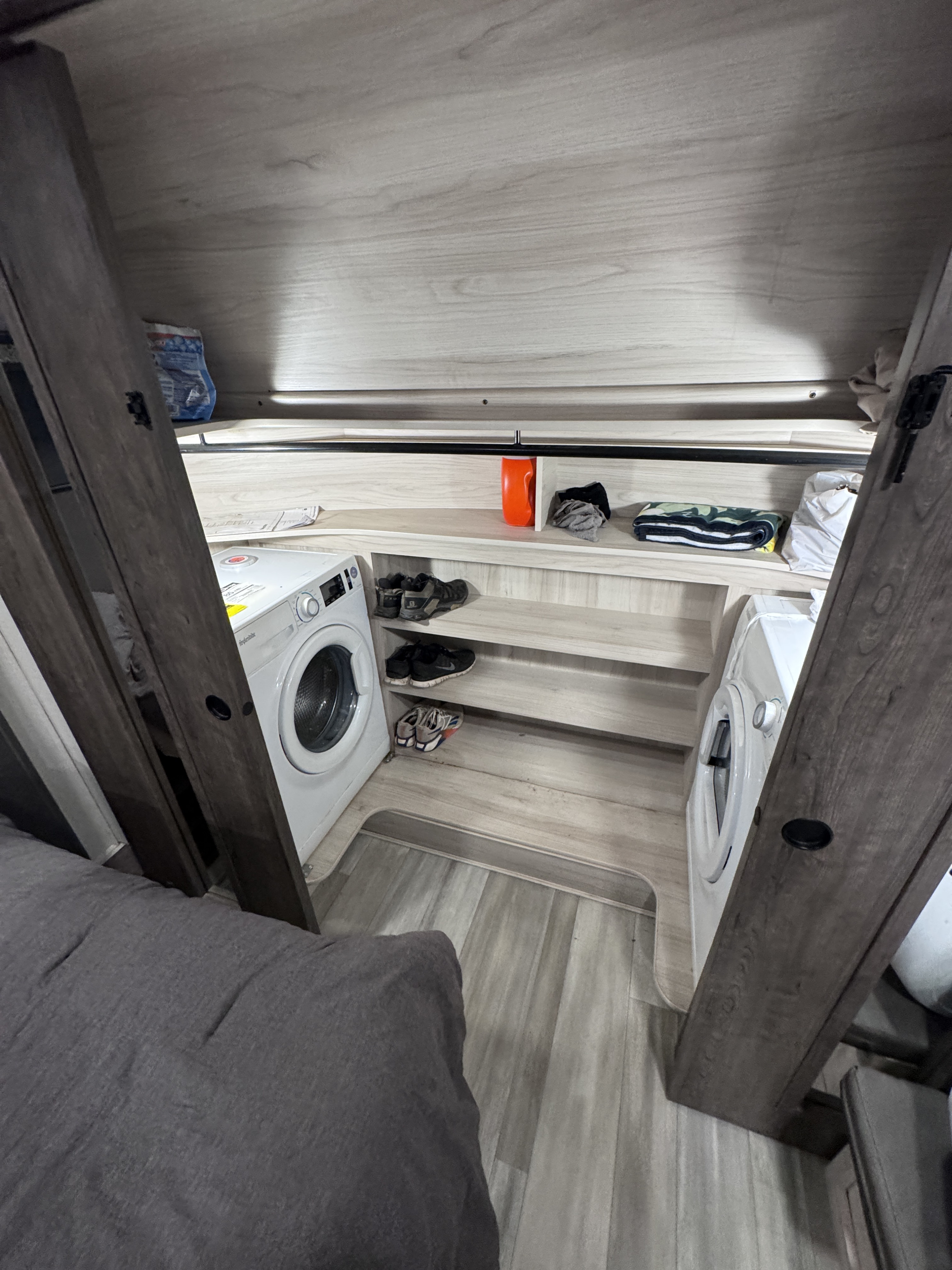 Compact RV rental laundry area with two front-load machines, shelved storage for shoes, clothes, and supplies.. Alliance RV Paradigm 2021
