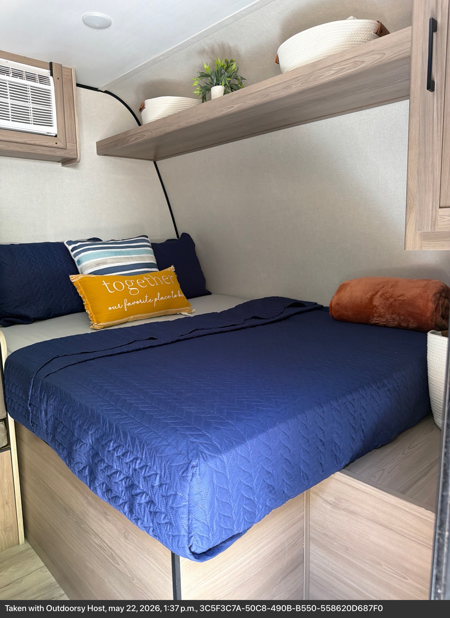 Inviting RV rental sleeping area with blue bedding, "together" pillow, AC unit, and storage shelves for comfort.. Keystone RV Coleman 2025