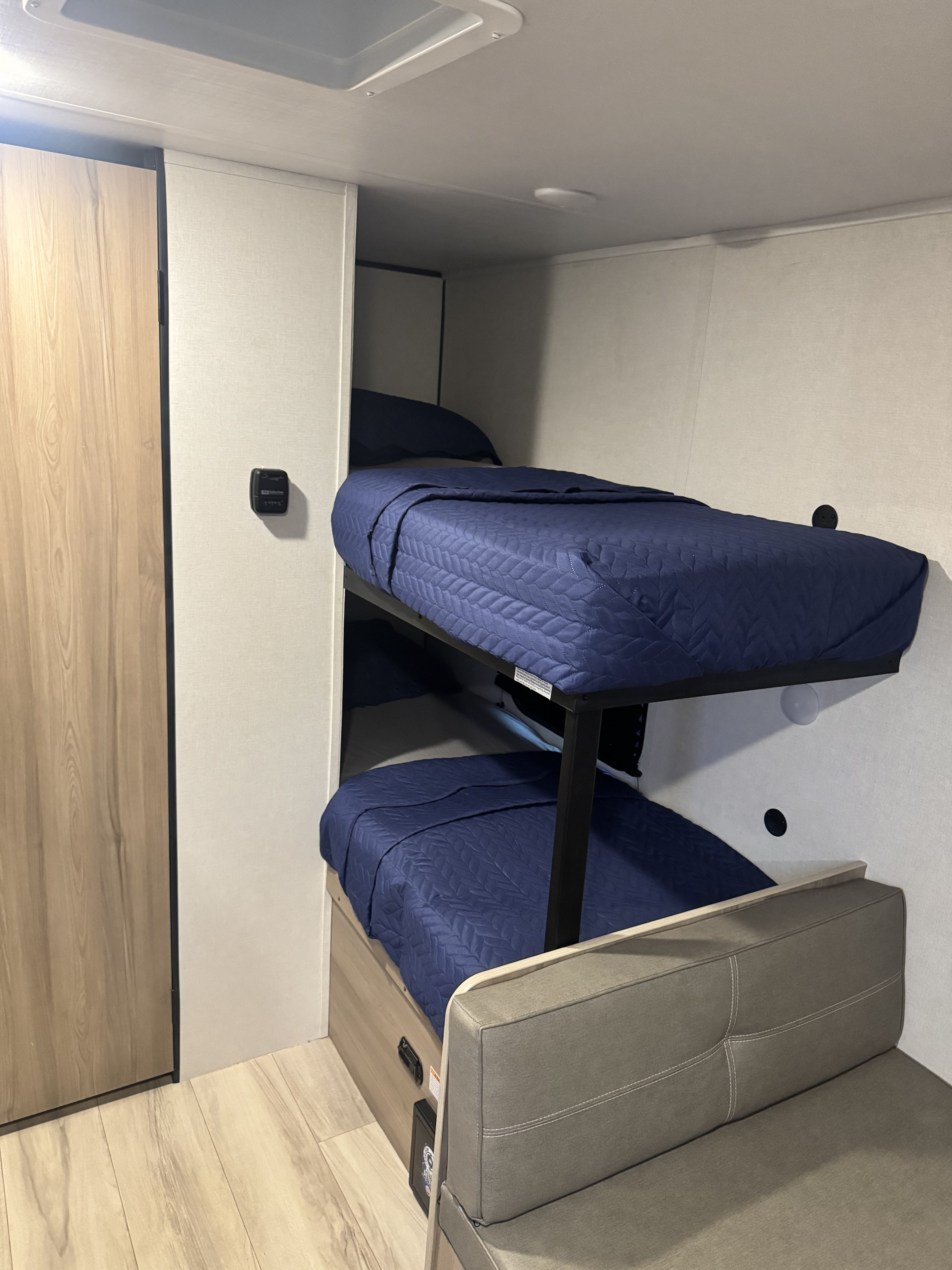 RV rental interior: cozy bunk beds with blue quilted bedding, a small closet, and a seating area for compact travel.. Keystone RV Coleman 2025