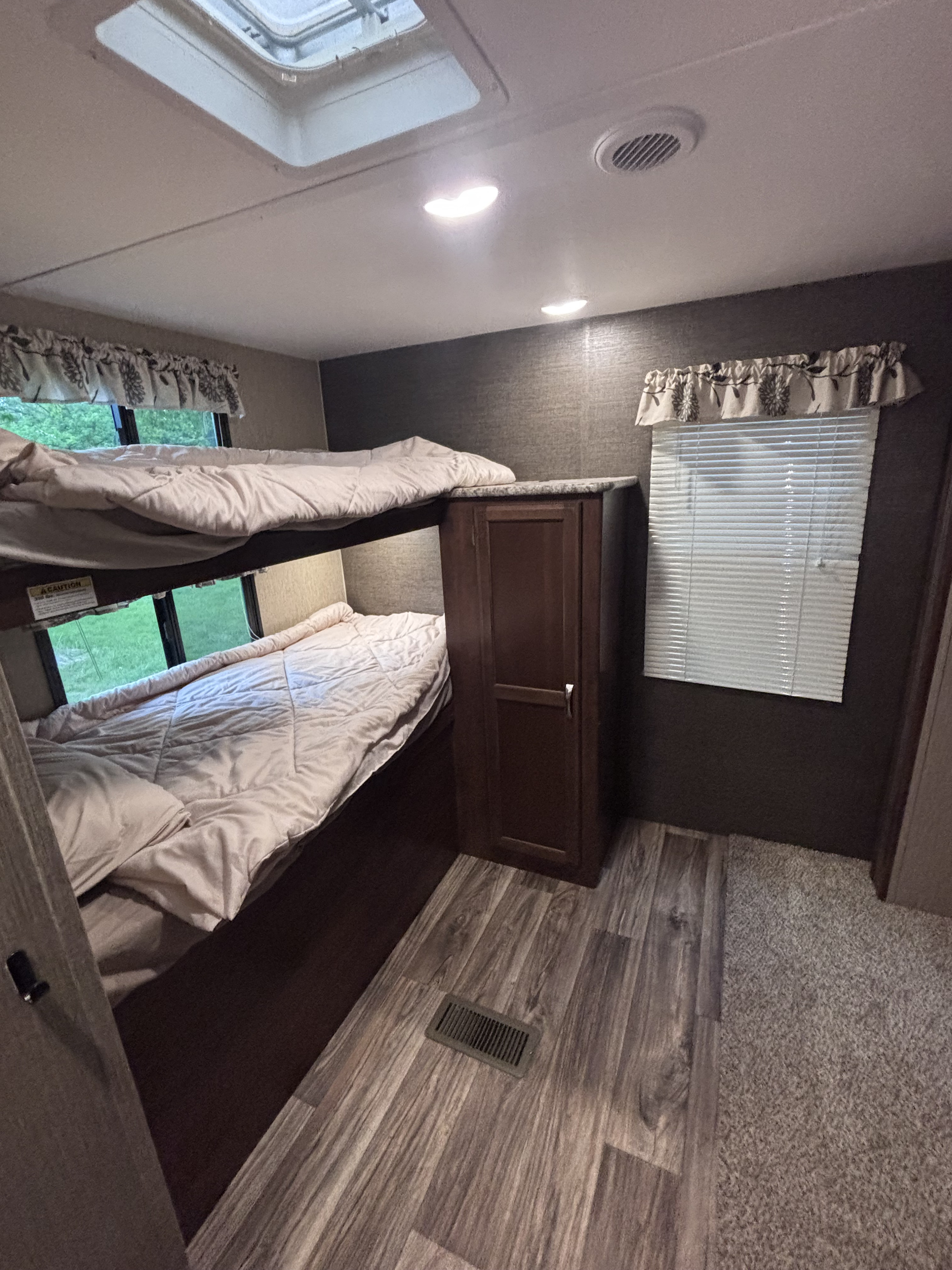 RV rental bunk beds: upper and lower bunks, windows, skylight, and storage cabinet, showcasing a cozy sleeping area.. Keystone RV Passport Grand Touring 2016