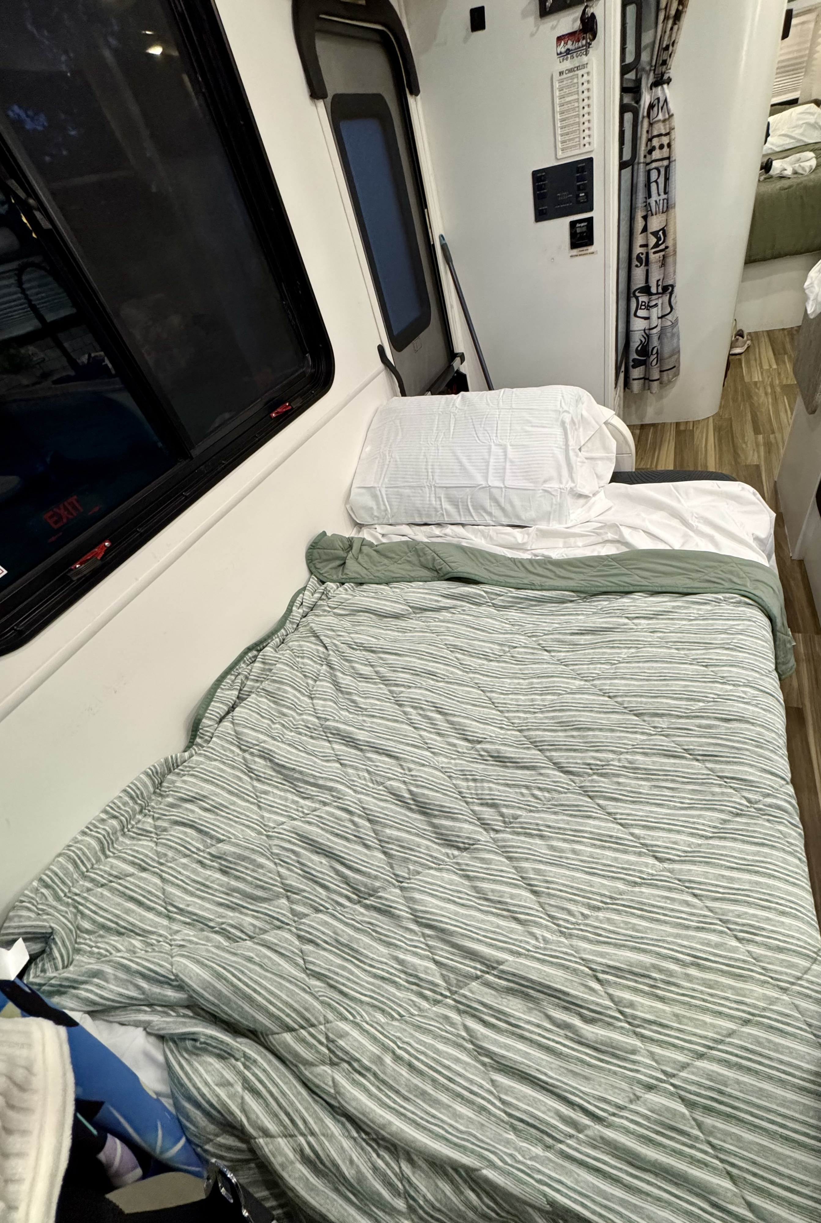 RV rental bedroom with a bed featuring striped green & white bedding, an exit window, and a wall-mounted RV checklist.. Forest River Coachmen Freelander 2017