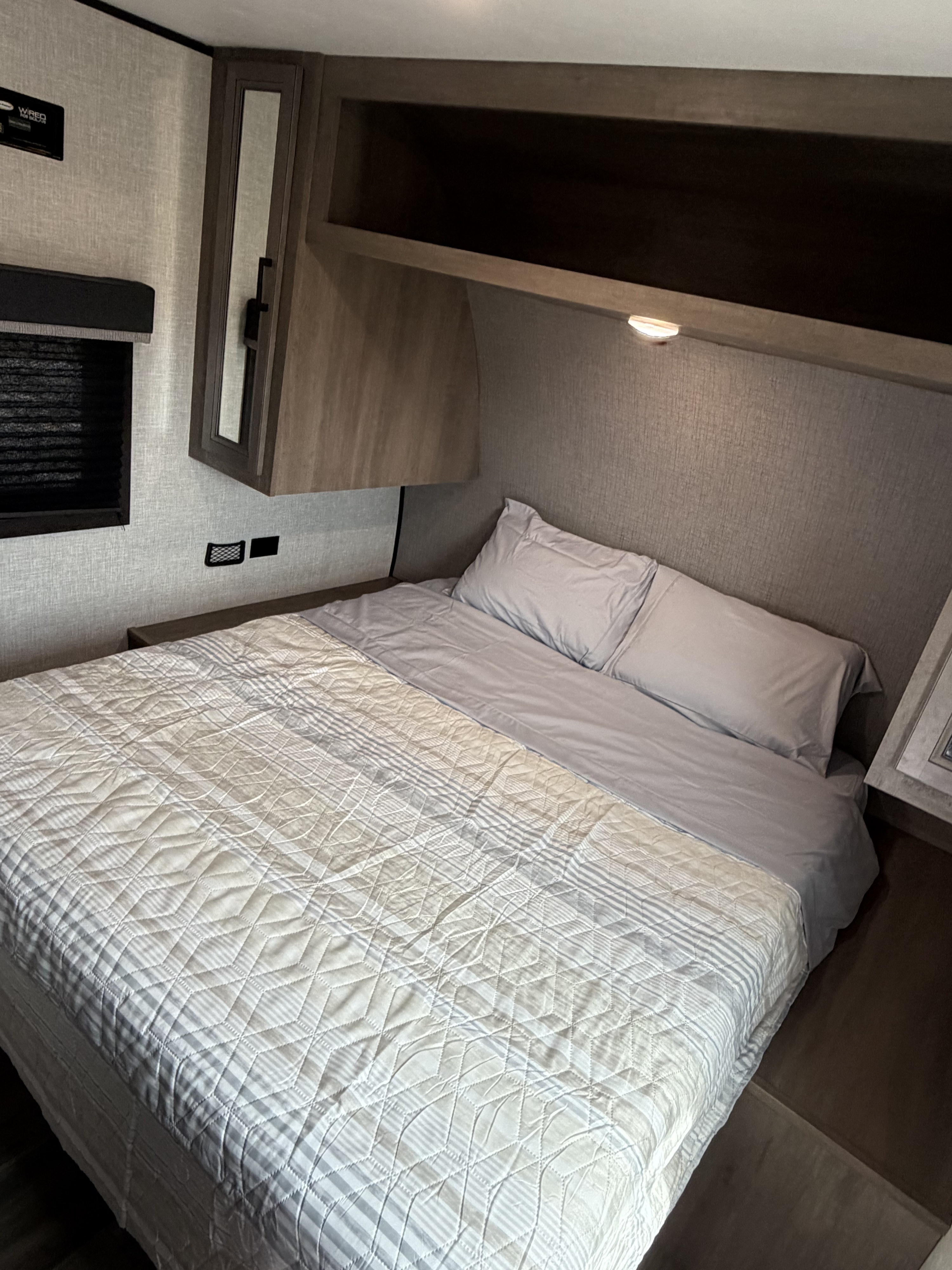 Cozy RV rental bedroom with a striped and quilted bed, overhead storage, and bedside charging, perfect for comfortable journeys.. Highland Ridge RV Open Range 2023