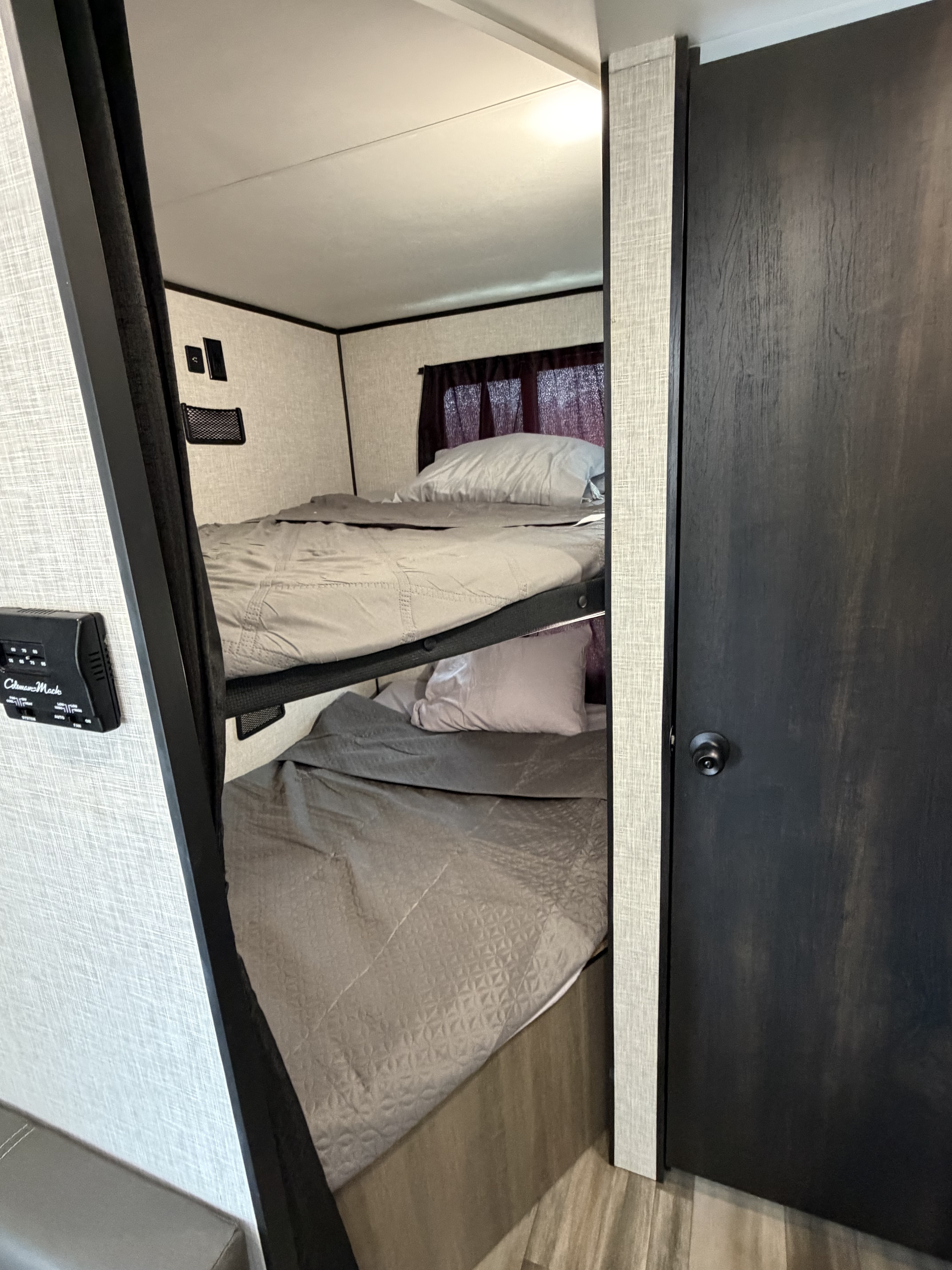 Compact rv rental bunk beds with gray bedding, a control panel, and a dark door, offering cozy sleeping in an RV interior.. Highland Ridge RV Open Range 2023