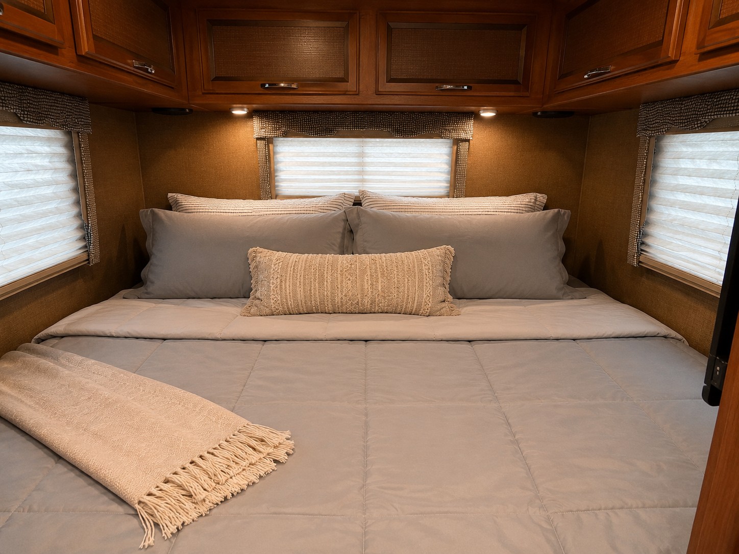 Cozy RV rental bedroom with comfortable bed, soft grey bedding, accent pillows, and overhead cabinets. Perfect for your next adventure.. Thor Vegas 2016