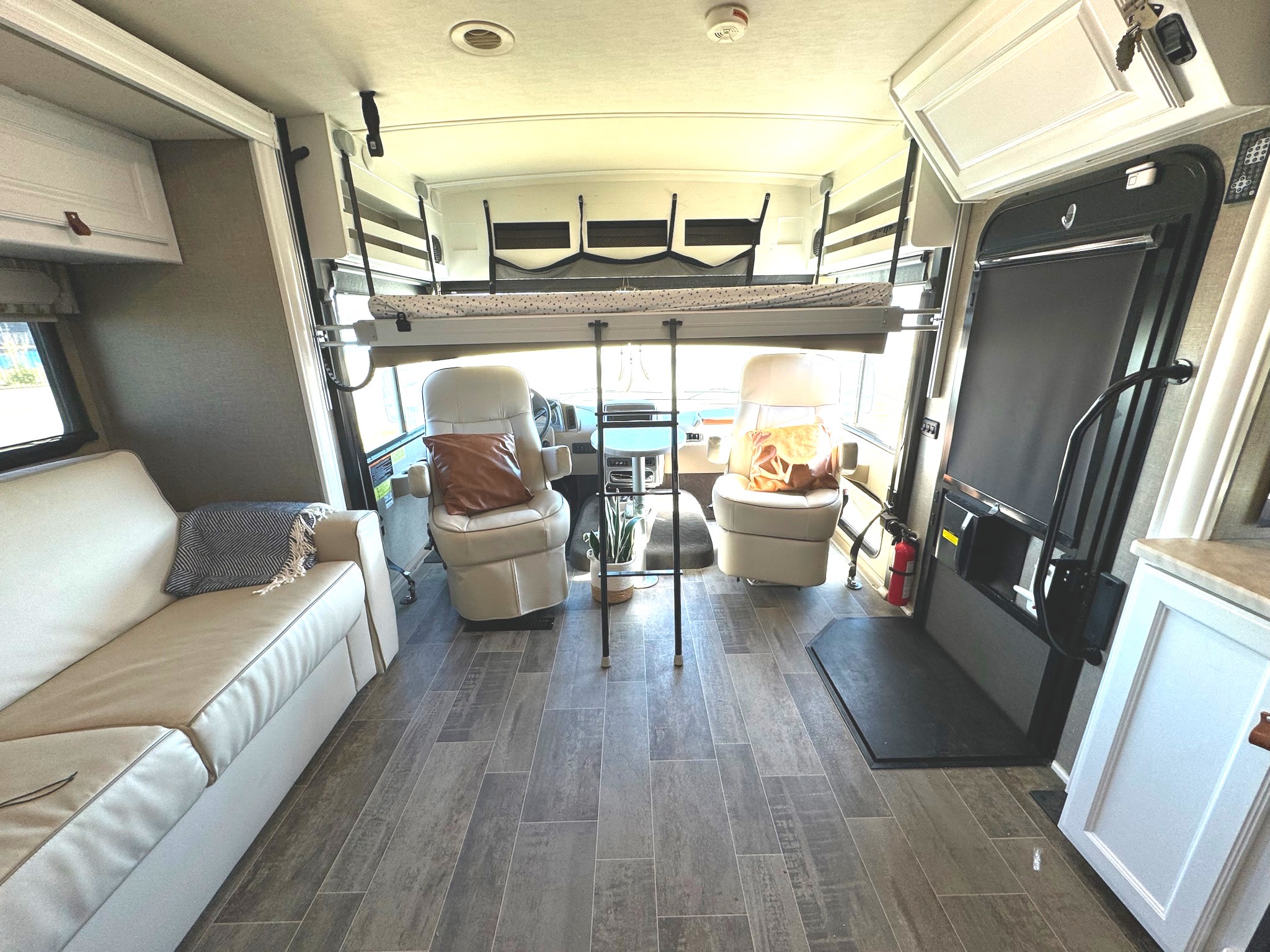 Experience comfort in this RV rental interior, showing a sofa, front cockpit with swiveling chairs, and an overhead bed.. Winnebago Adventurer 2020