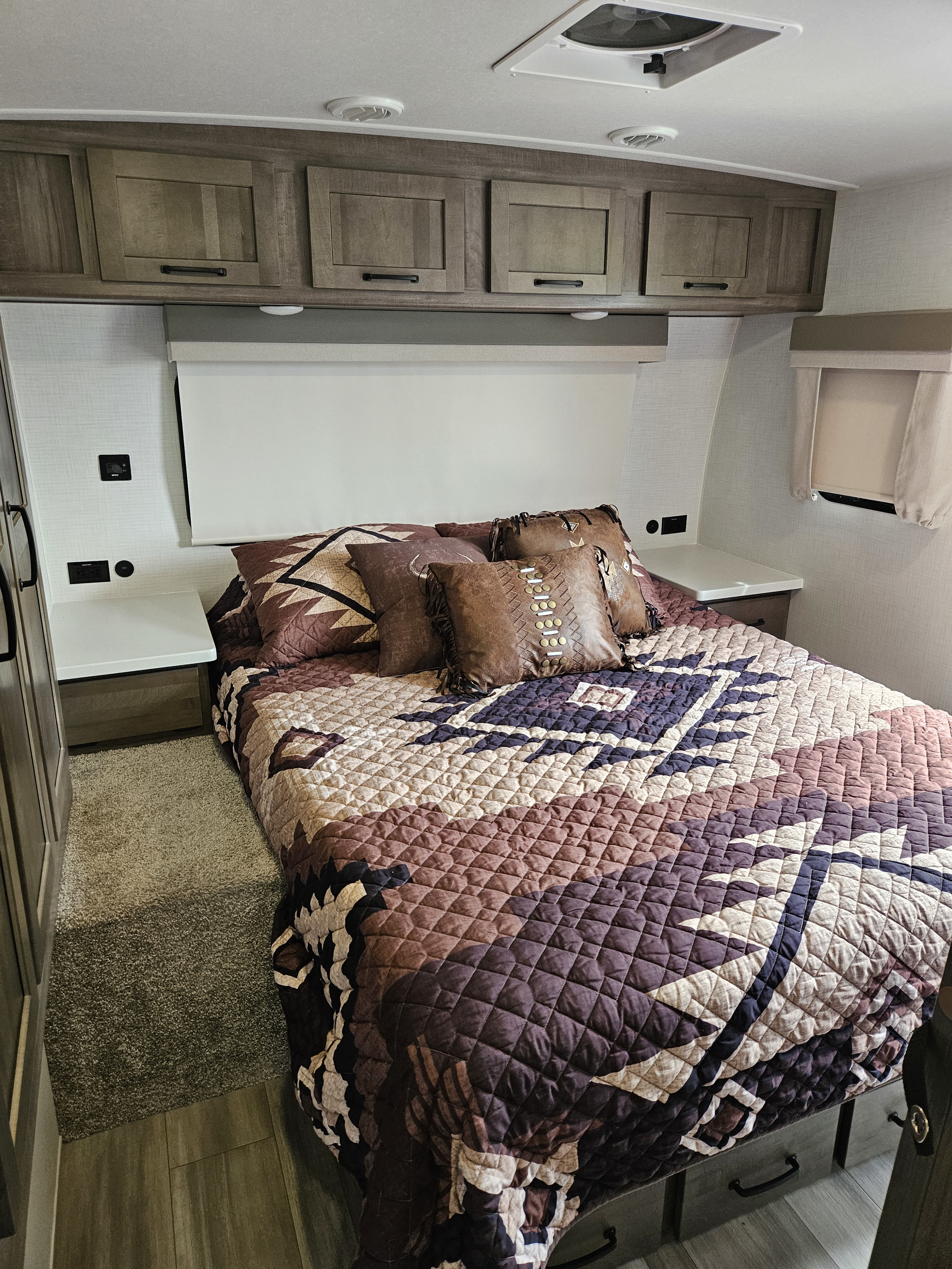 Cozy RV rental bedroom with patterned bedding, leather pillows, overhead cabinets, and bedside charging for a comfortable stay.. Forest River Flagstaff Super Lite 2024