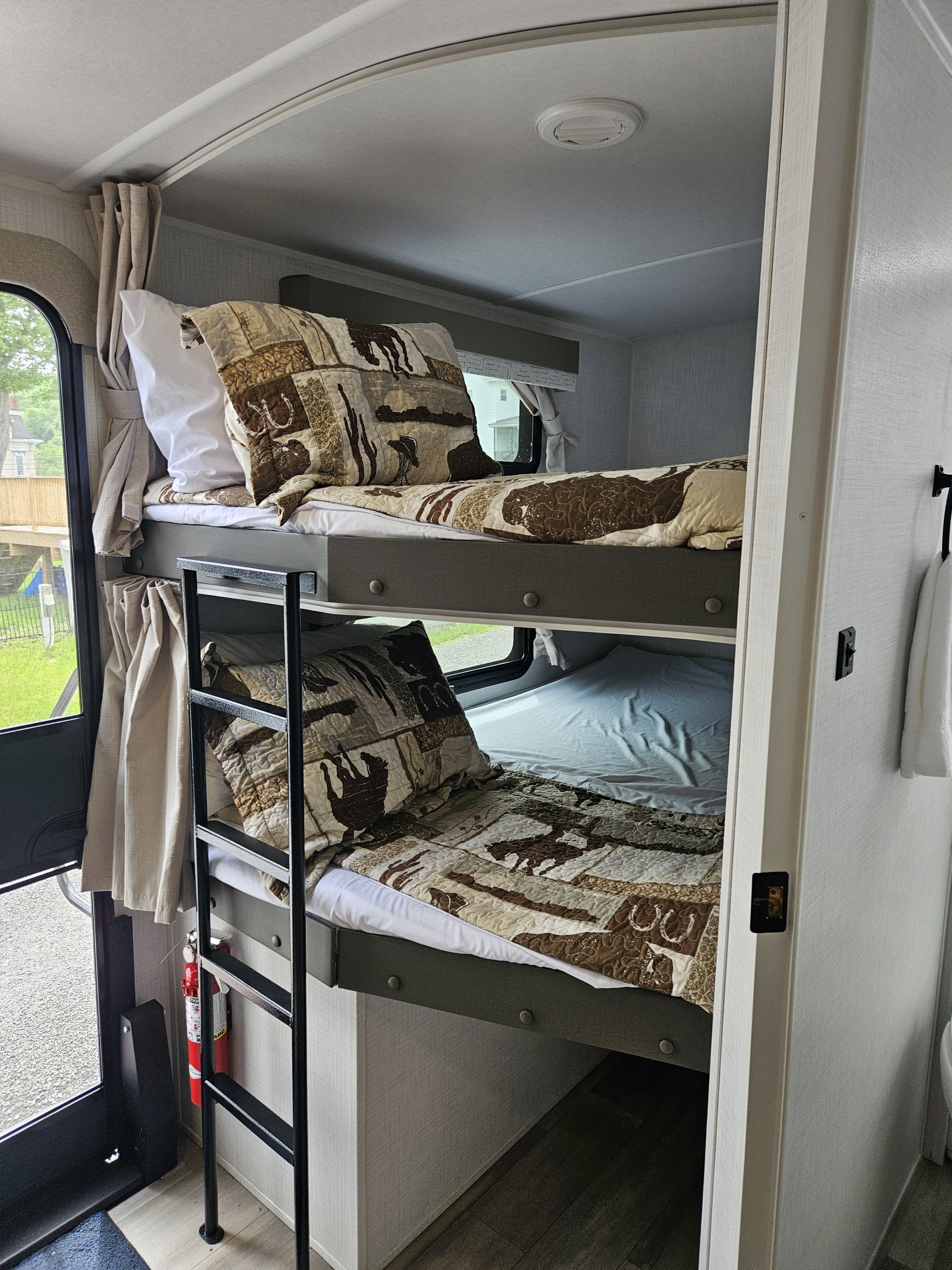 Inside an RV rental: two bunk beds with Western-themed bedding, a safety ladder, window views, and a fire extinguisher.. Forest River Flagstaff Super Lite 2024