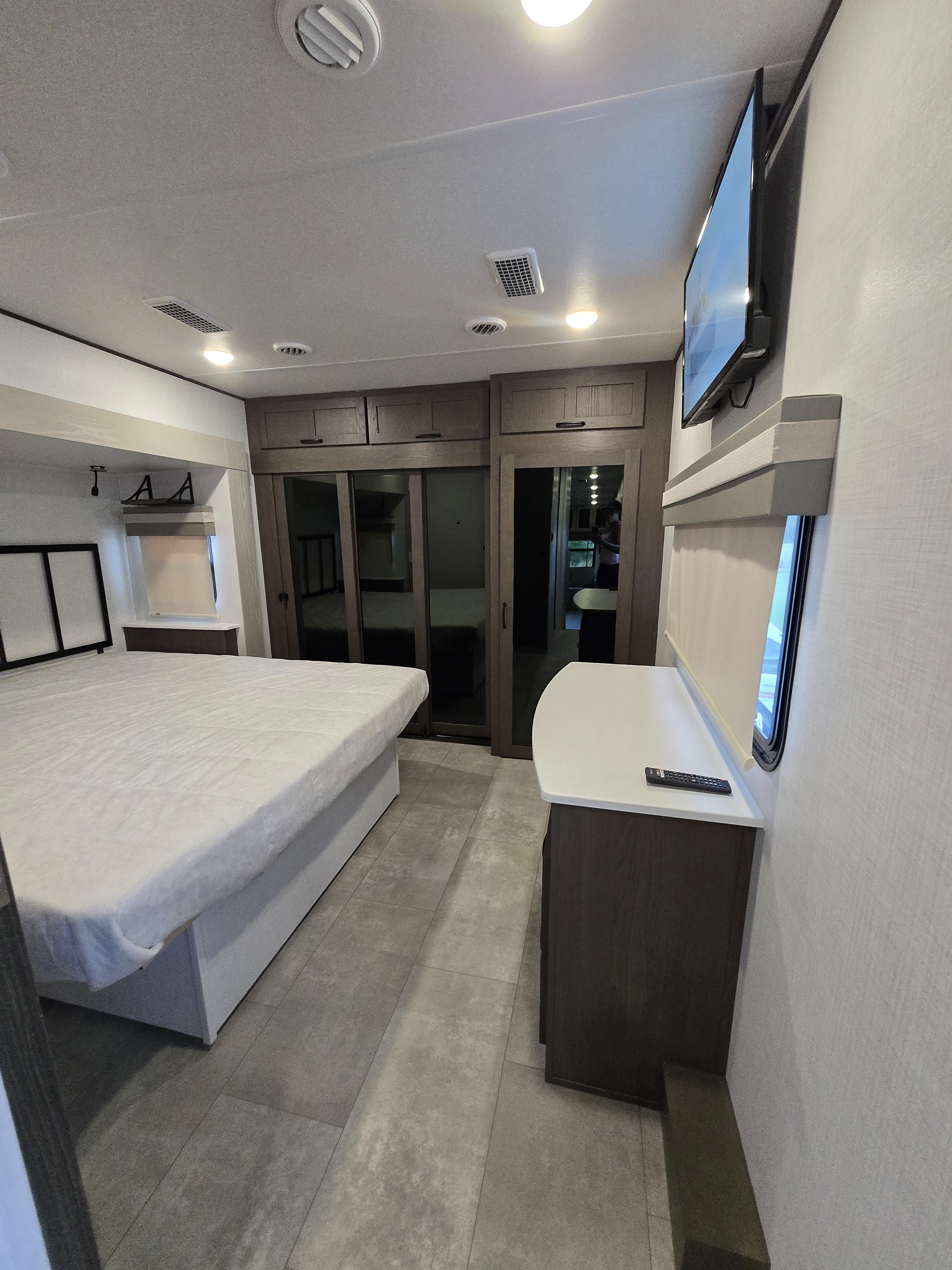 Modern RV rental bedroom featuring a queen bed, mirrored wardrobes, wall-mounted TV, dresser, and sleek tile flooring.. Forest River Palomino Columbus 2024