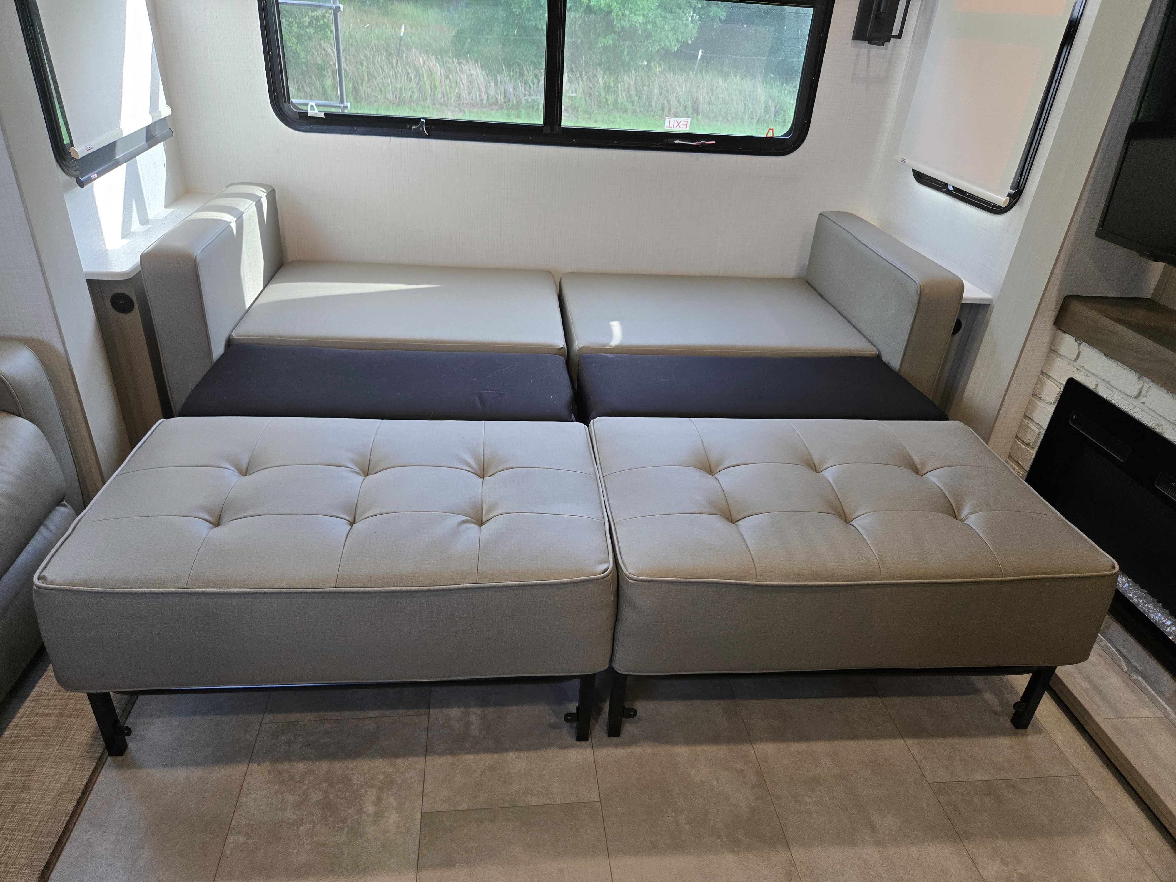 This RV rental features a comfortable convertible sofa that transforms into a bed, with matching tufted ottomans. Exit sign visible.. Forest River Palomino Columbus 2024