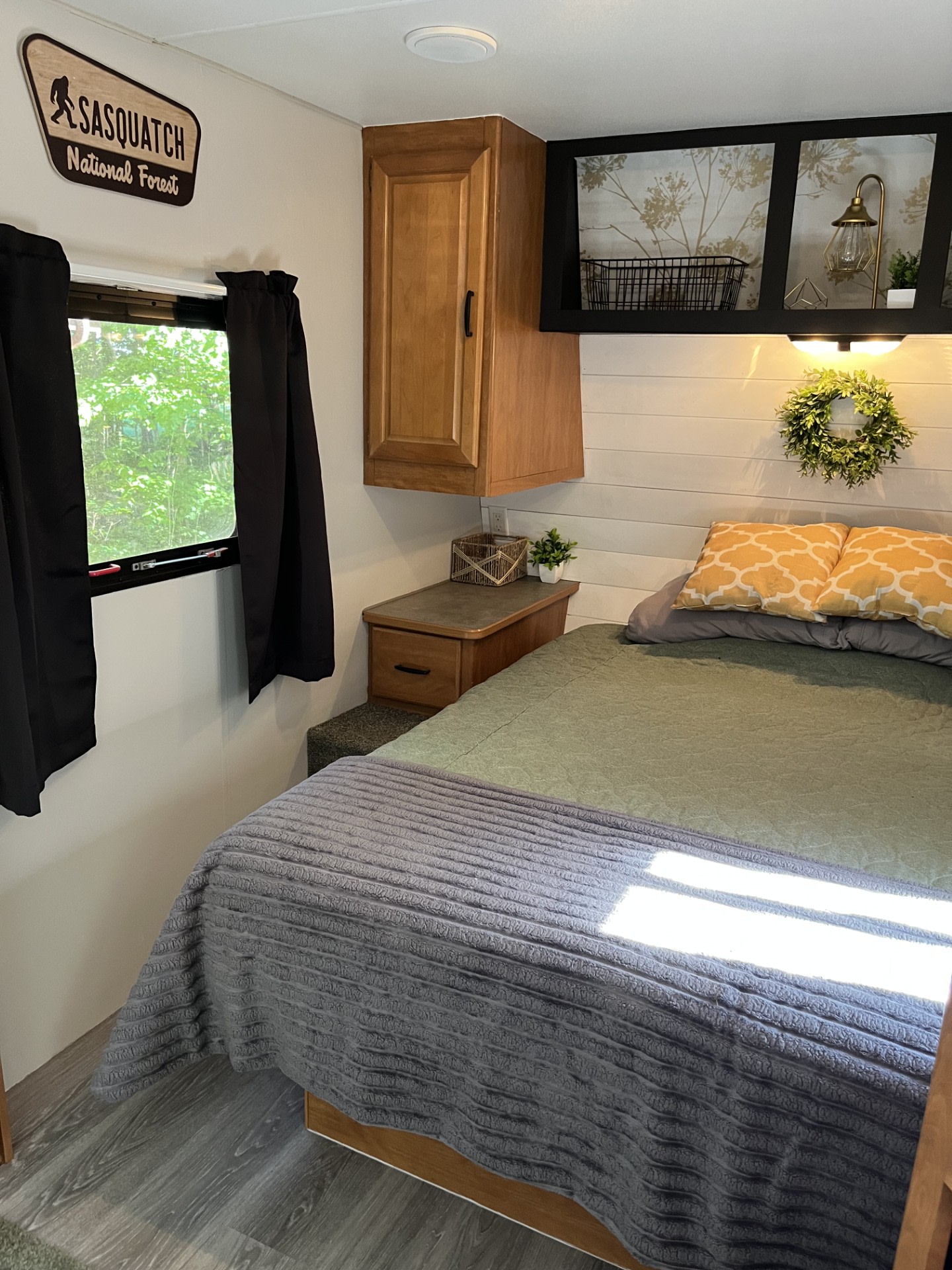 Inside a cozy rv rental bedroom: green comforter, yellow pillows, Sasquatch sign, shiplap headboard, and wood-look floor.. Wilderness Wilderness Trailer 2006