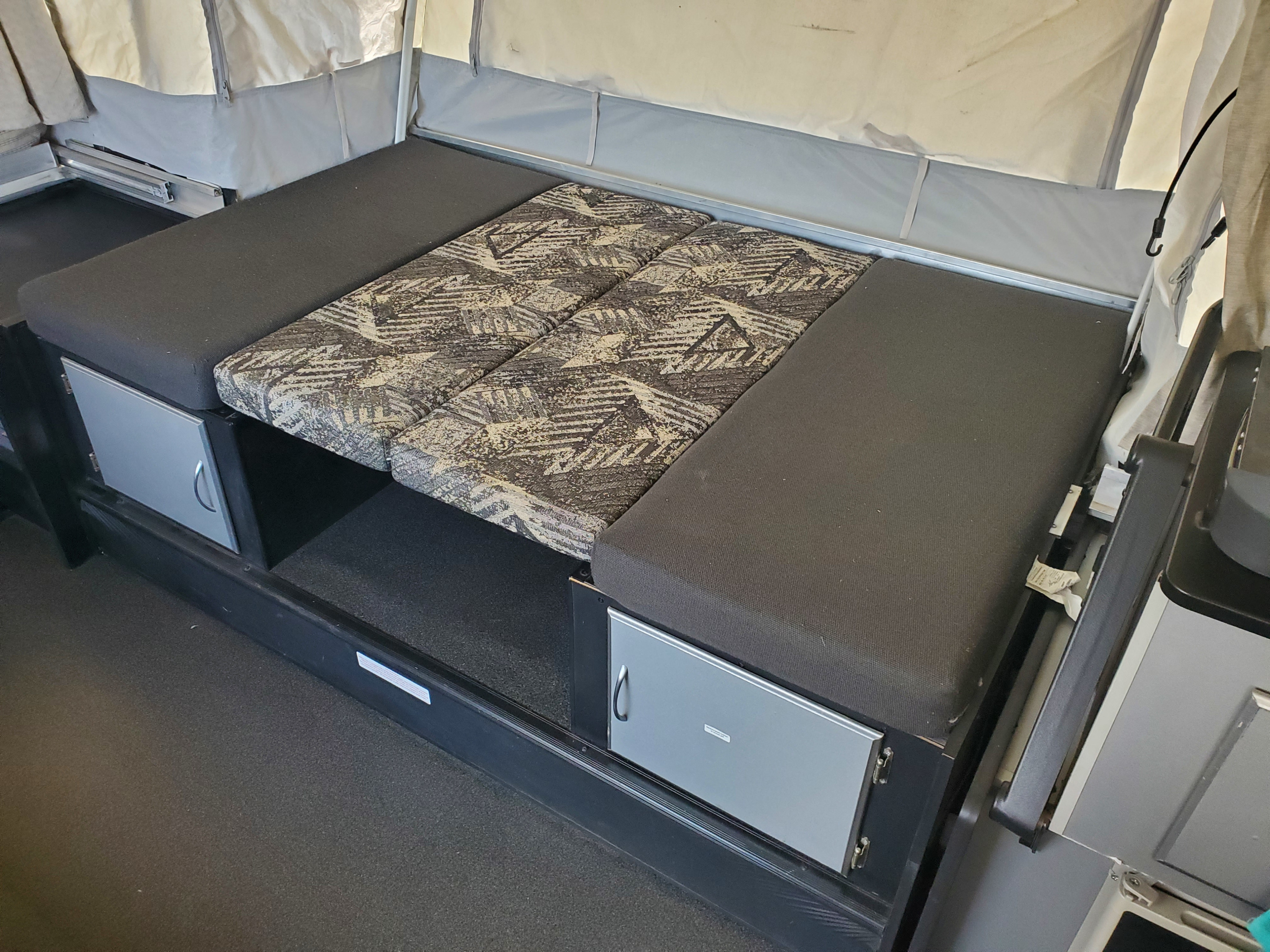 RV rental pop-up camper interior, showing modular seating with patterned and dark cushions, and built-in storage compartments.. Fleetwood Evolution 2008
