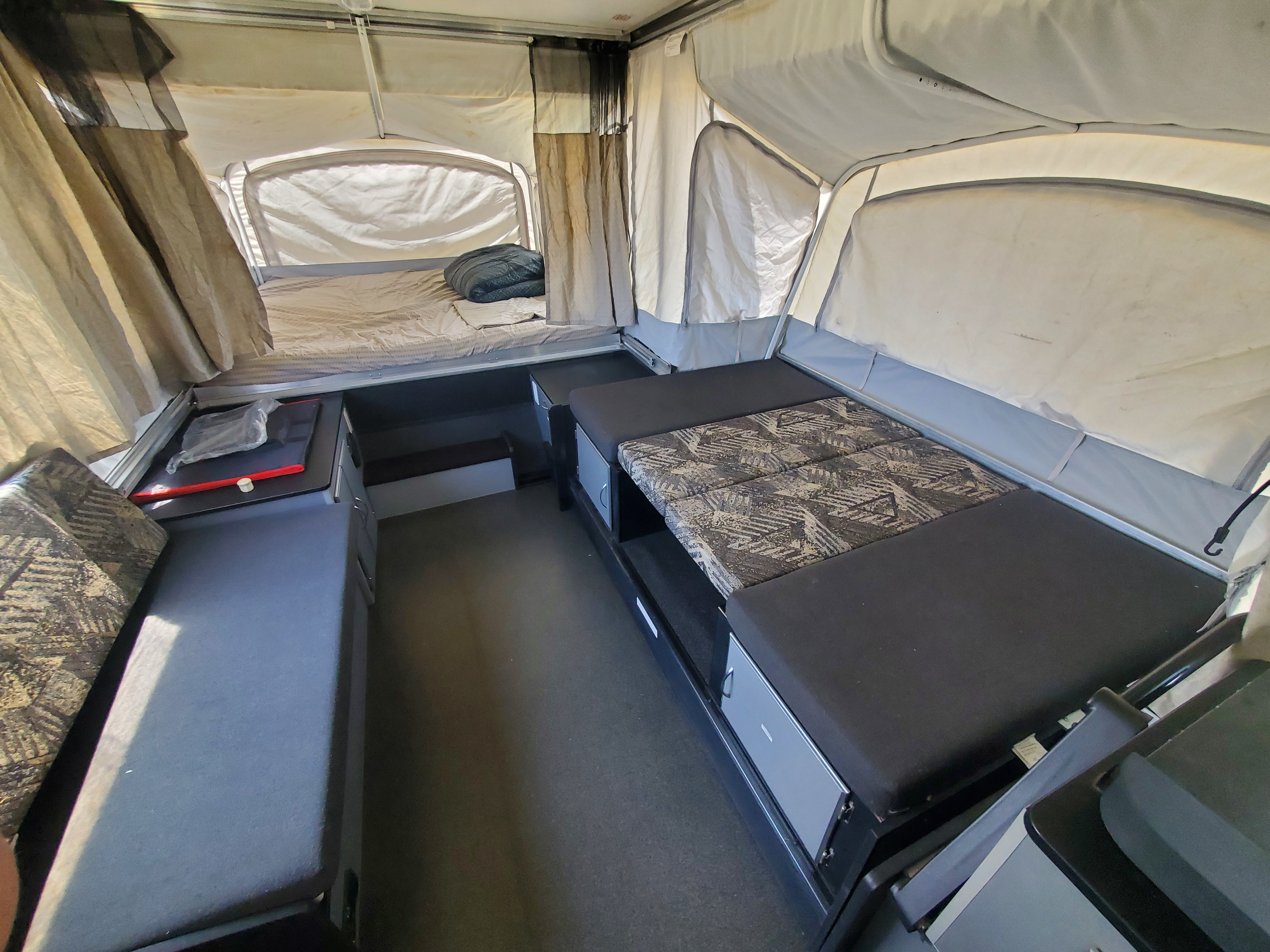 Inside an RV rental pop-up camper: two beds, patterned seating, and built-in storage. Ideal for camping adventures.. Fleetwood Evolution 2008
