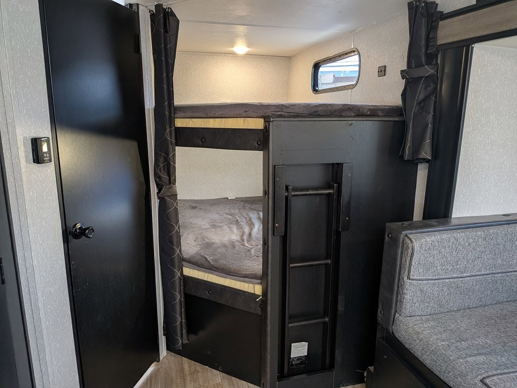 This RV rental interior features dark bunk beds with a ladder, a small window, and a gray seating area.. Forest River Cherokee Grey Wolf 2022