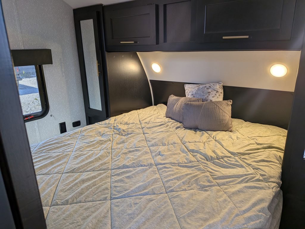 Cozy RV rental bedroom featuring a comfortable bed with light comforter, dark overhead cabinets, window, and bedside lights.. Forest River Cherokee Grey Wolf 2022