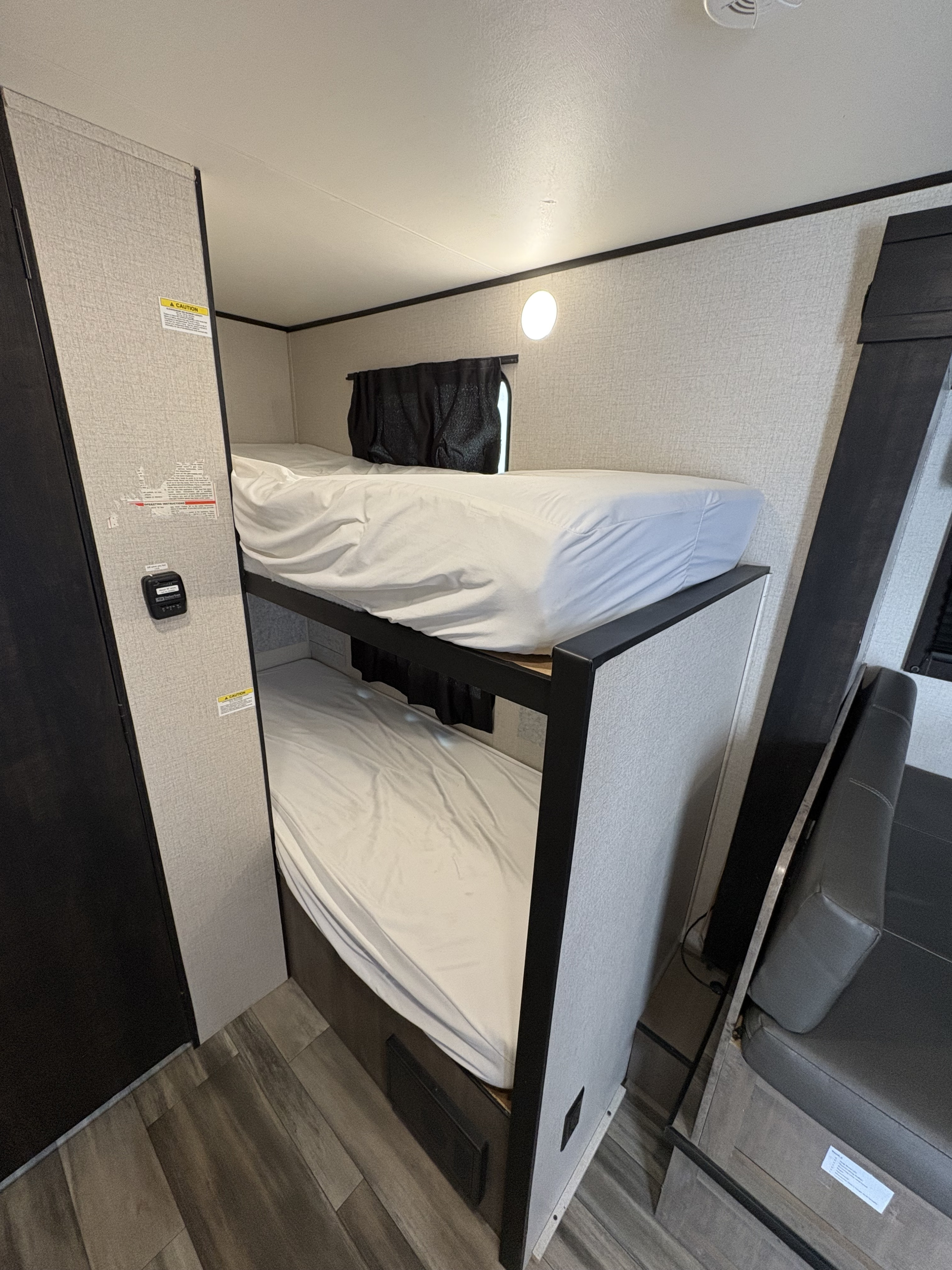 RV rental interior view: two bunk beds with white sheets, a window with a dark curtain, and wood-look flooring.. Highland Ridge RV Open Range 2022