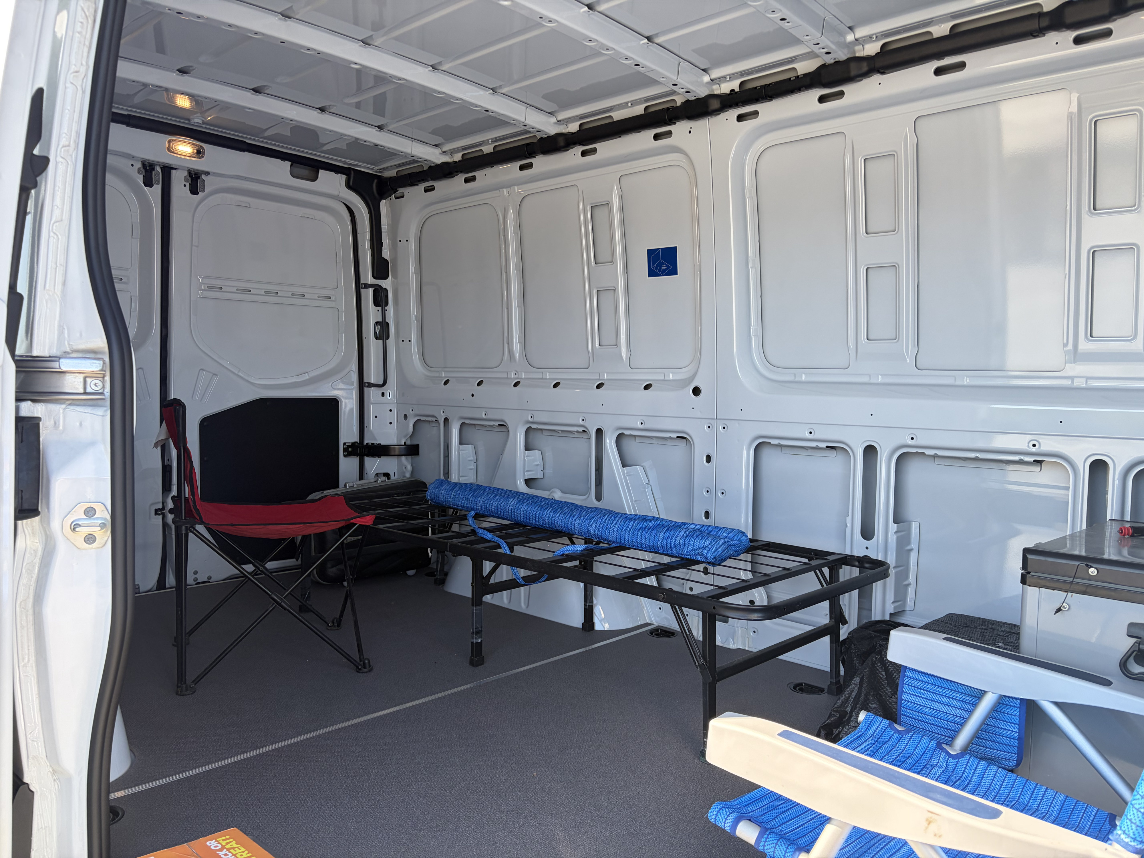 Inside this rv rental: a cargo van interior with a cot, chairs, and cooler, ready for camping adventures.. Mercedes-Benz Sprinter 2025