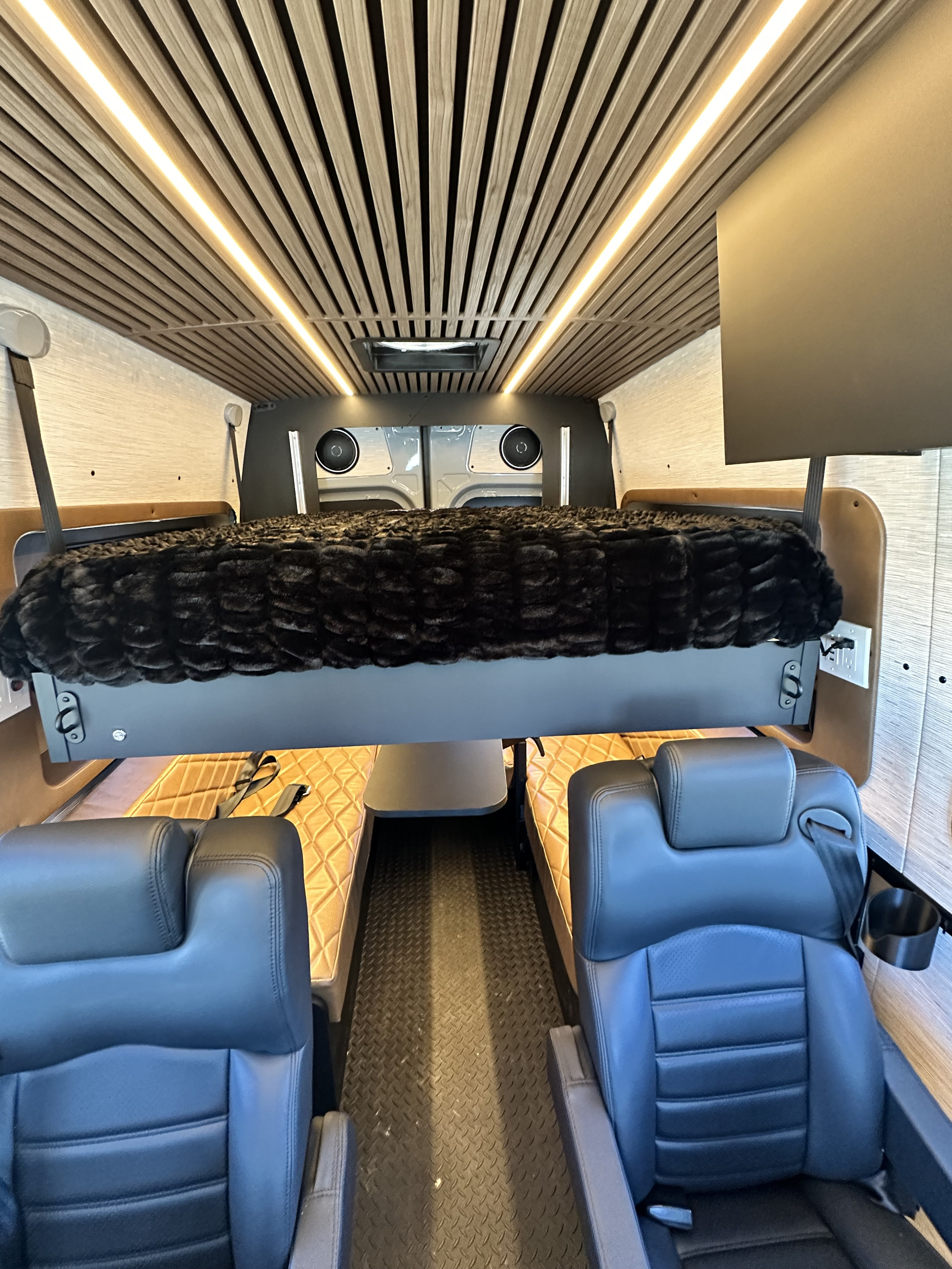 Stylish RV rental interior: elevated bed with furry blanket, comfy captain seats, and slatted ceiling with LED lighting.. Rogue Van Rogue Van Class B 2025