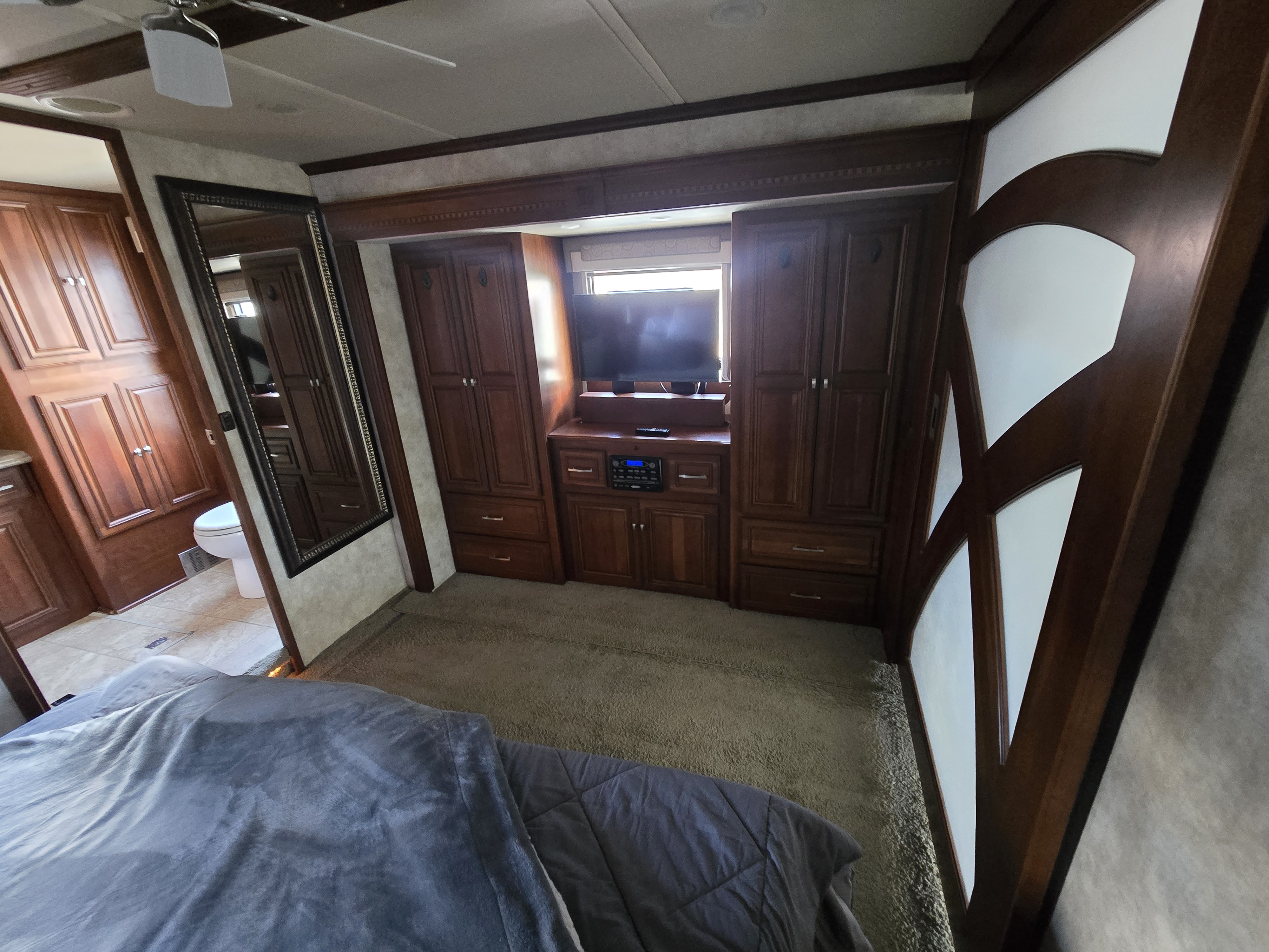 Spacious RV rental bedroom with rich wood cabinetry, entertainment center, TV, and comfortable bed, featuring an attached bathroom.. Winnebago Tour 2011