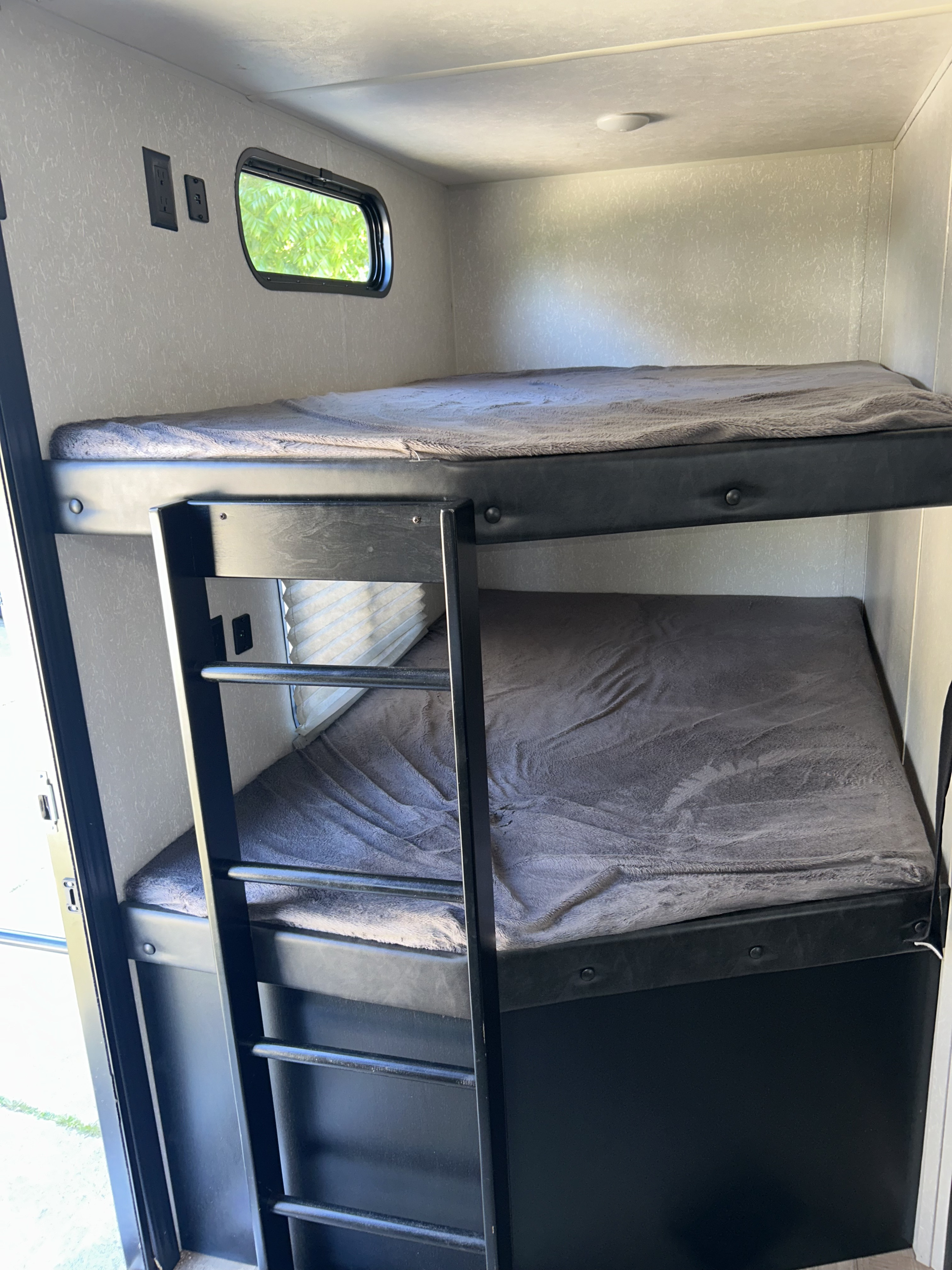 Inside an rv rental: dark-framed bunk beds with grey blankets. A small window, wall outlets, and ceiling light create a functional sleeping area.. Forest River Cherokee Grey Wolf Special Edition 2021