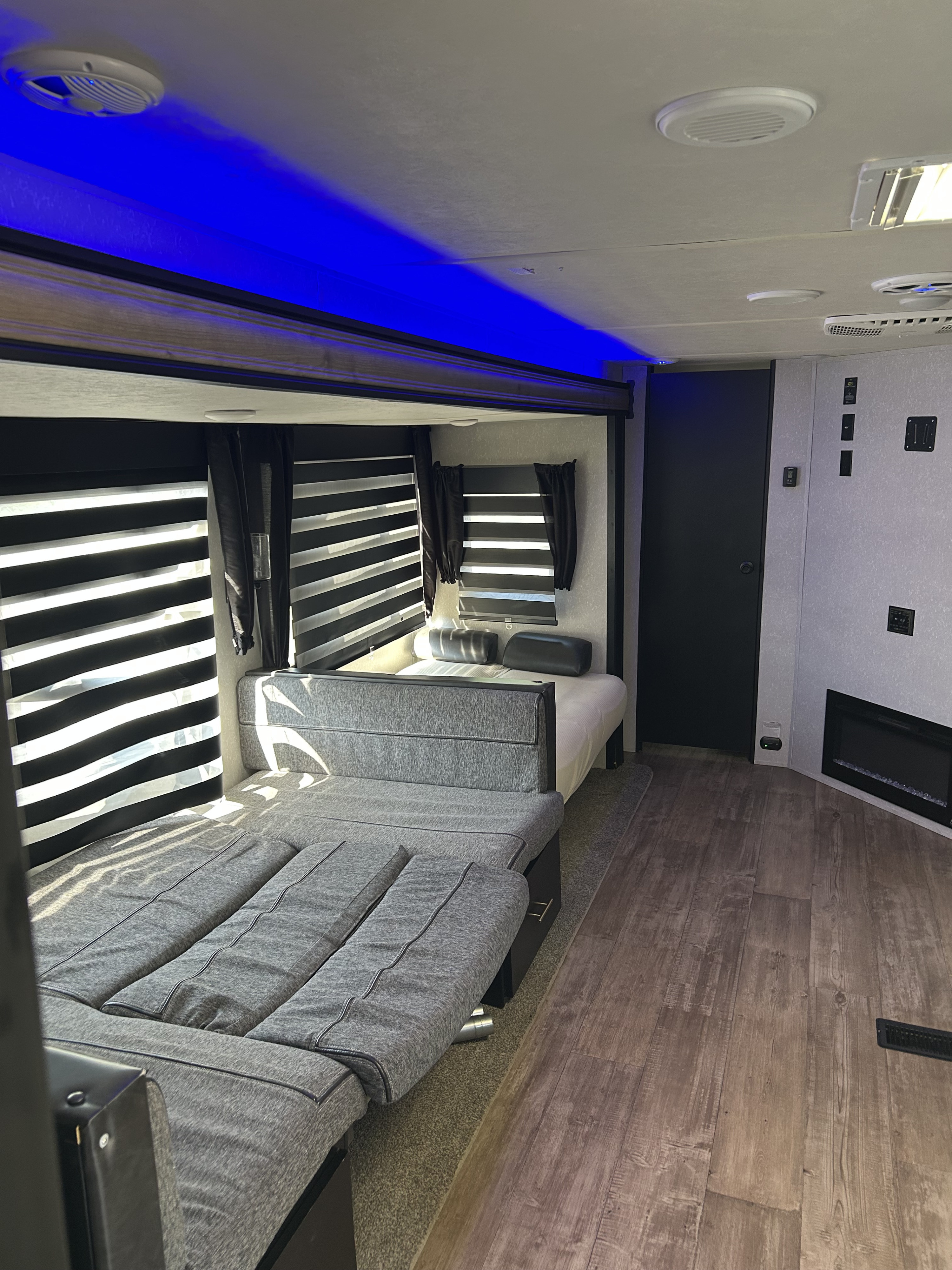 Spacious rv rental interior showing a gray convertible sofa bed, fixed bed, modern blue ceiling lights, and wood-look floors.. Forest River Cherokee Grey Wolf Special Edition 2021