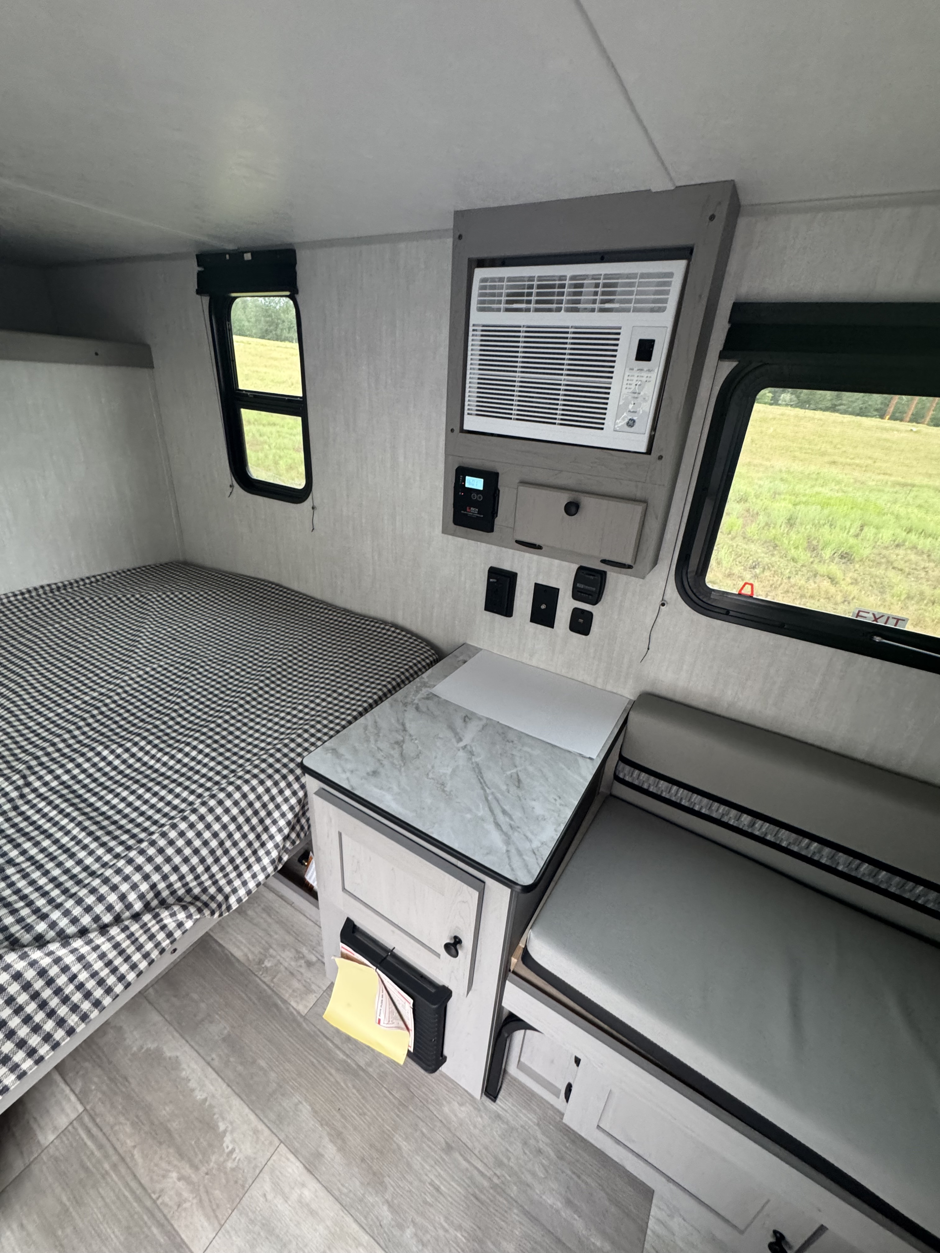 This RV rental's interior boasts a comfortable bed, wall-mounted AC unit, dinette, and bright windows with green outdoor scenery.. Forest River Forest River Aurora ROK 12ROK 2025