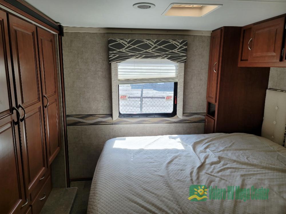 Inside an RV rental bedroom showing a bed, window with blinds, overhead light, and wooden cabinets.. Itasca Spirit 2014