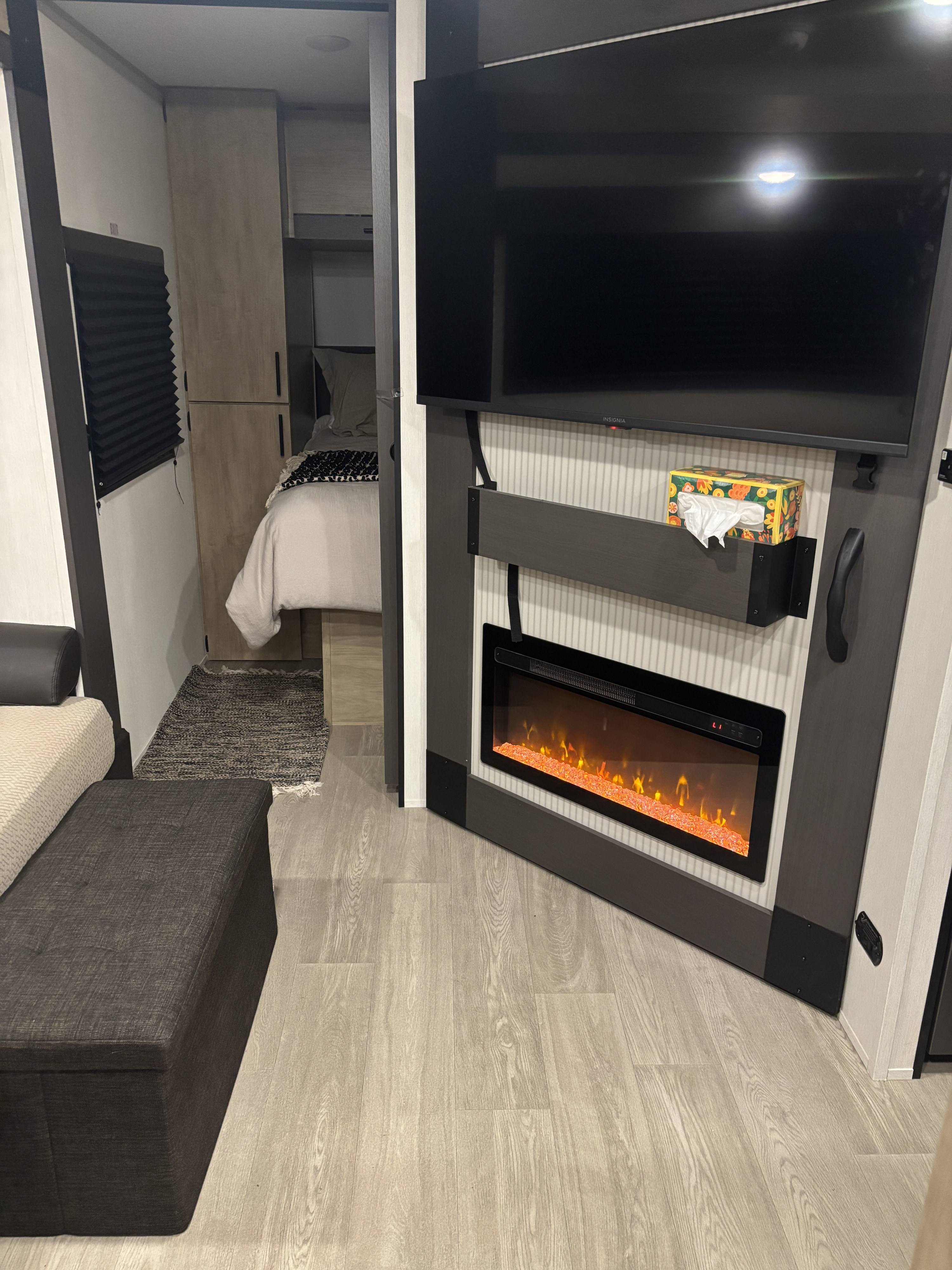 Cozy RV rental interior: living area with a TV, electric fireplace, and a connected bedroom, all on light wood flooring.. Forest River Campsite Reserve 2026