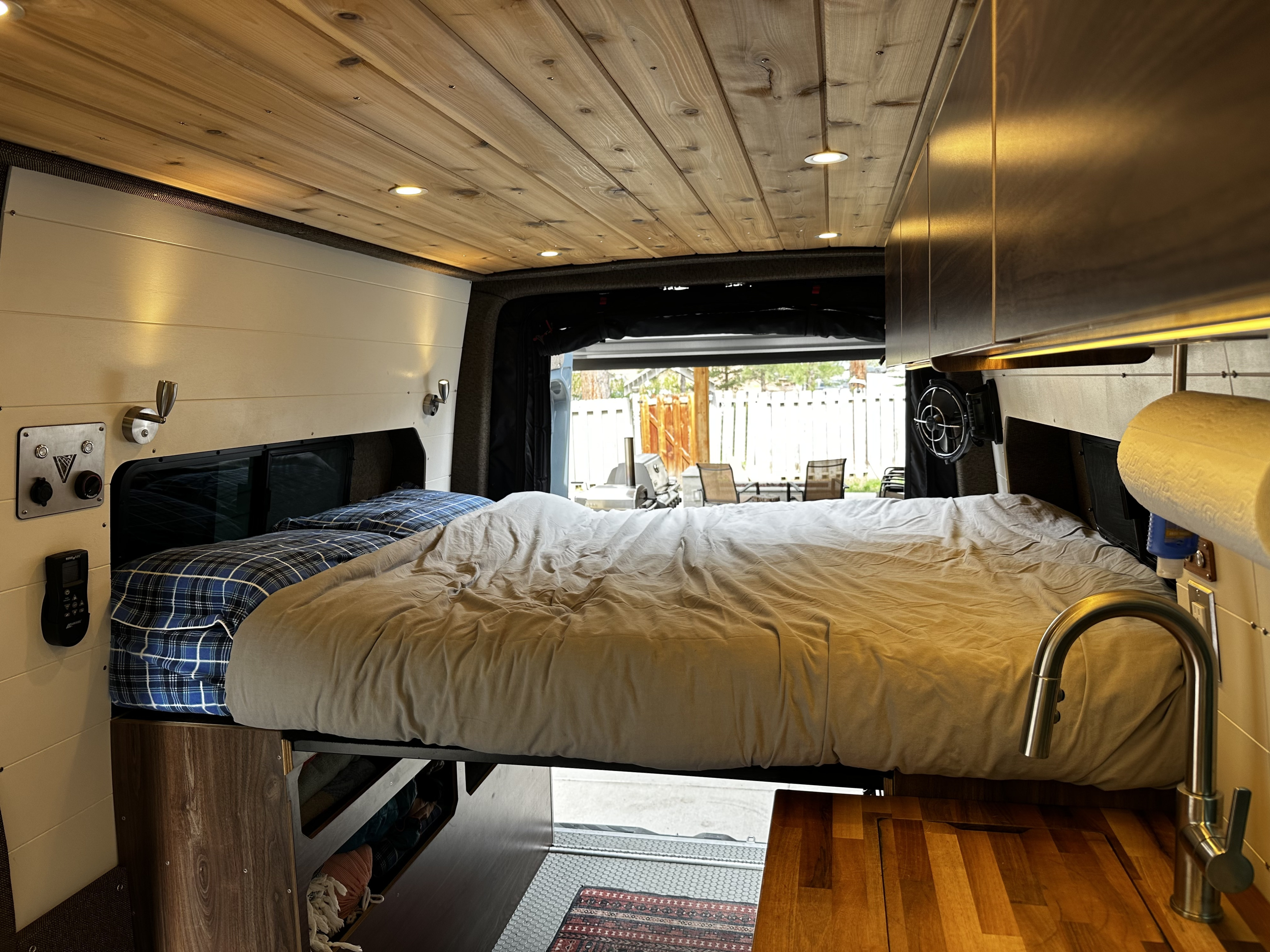 Cozy RV rental interior: bed, wooden ceiling, compact kitchenette, and view of outdoors from open back.. Mercedes-Benz Sprinter 2020