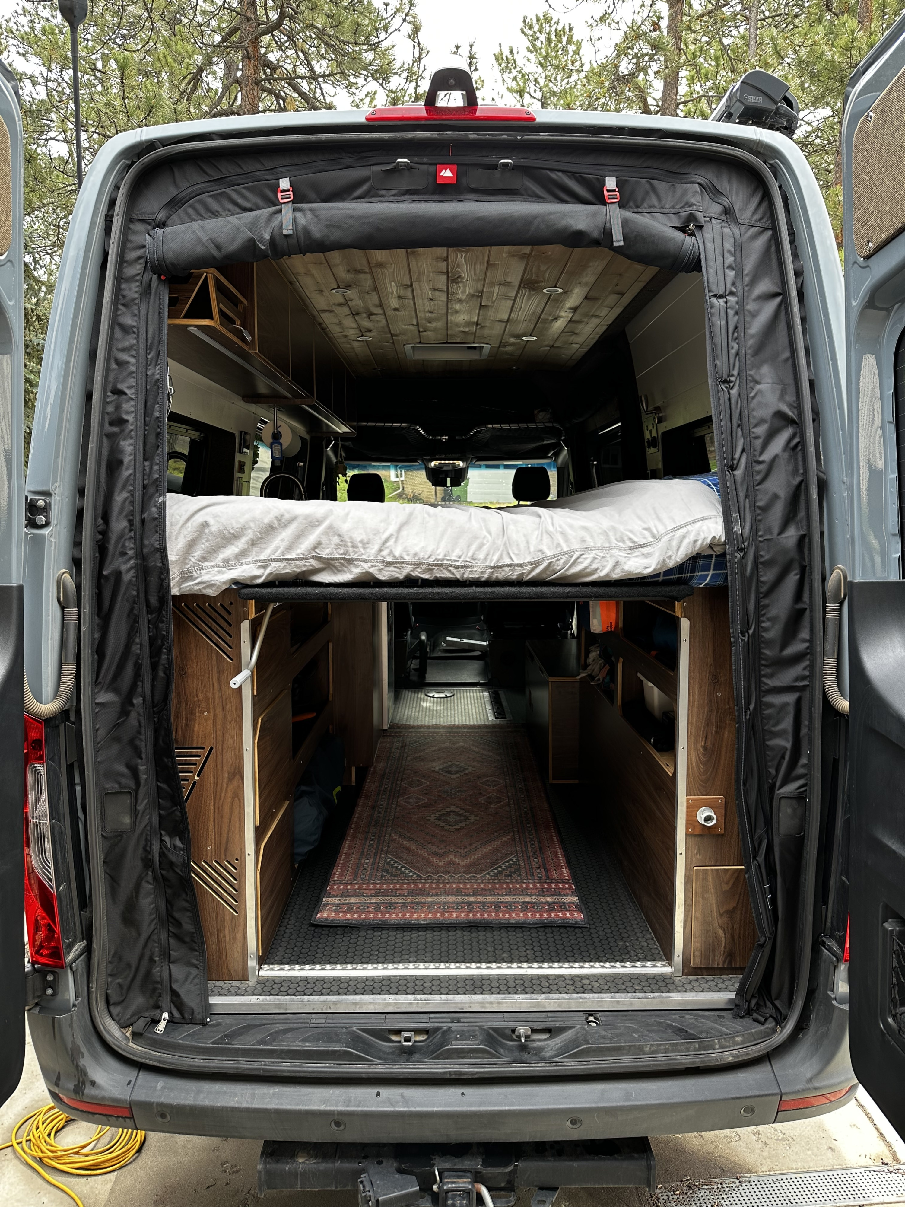 Step into your next rv rental adventure! Rear view of a custom camper van interior with a raised bed, storage, and cozy rug.. Mercedes-Benz Sprinter 2020