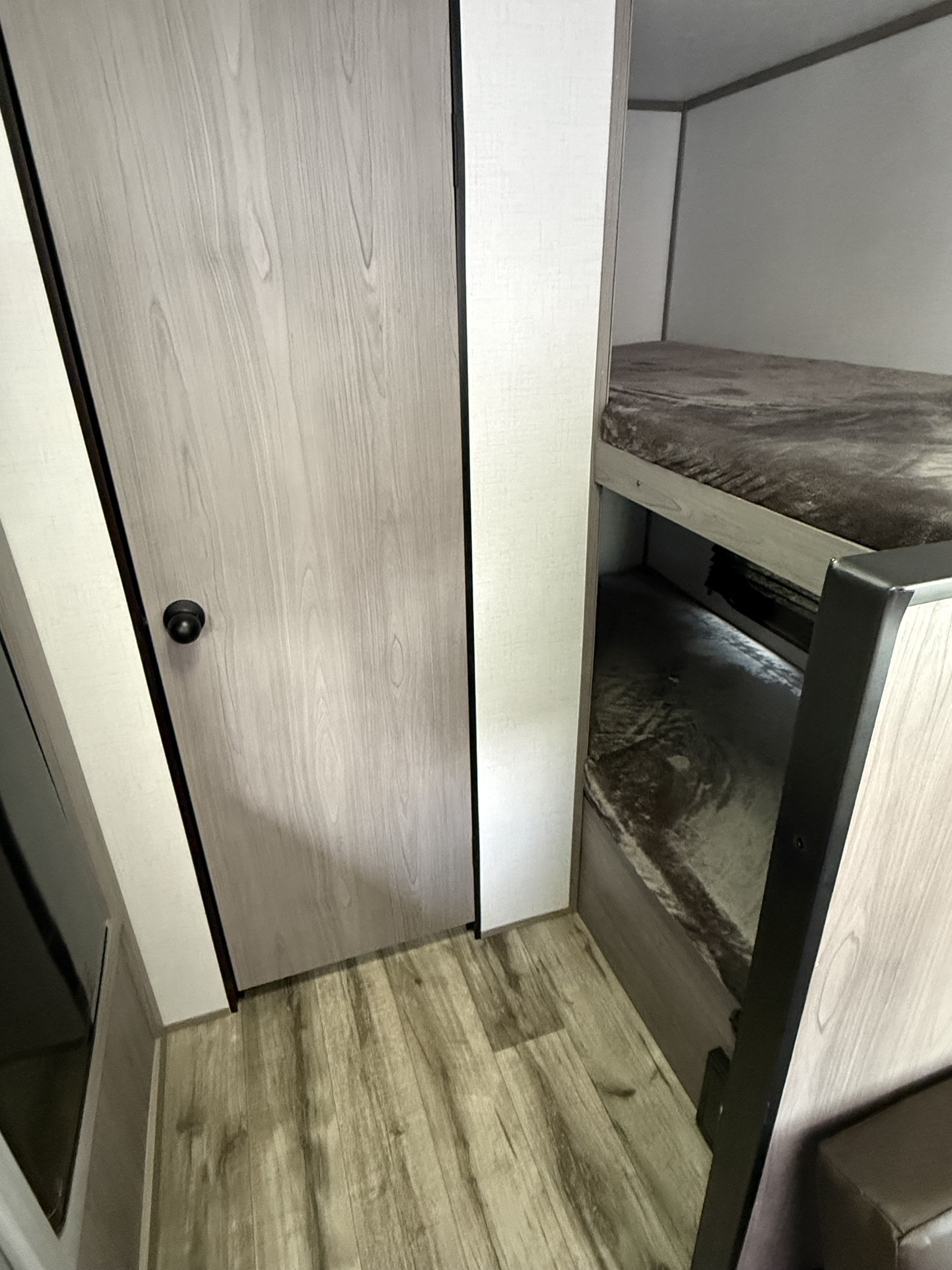 RV rental interior showcasing cozy bunk beds, light wood door, and compact sleeping design.. Dutchmen Coleman Lantern LT 2023