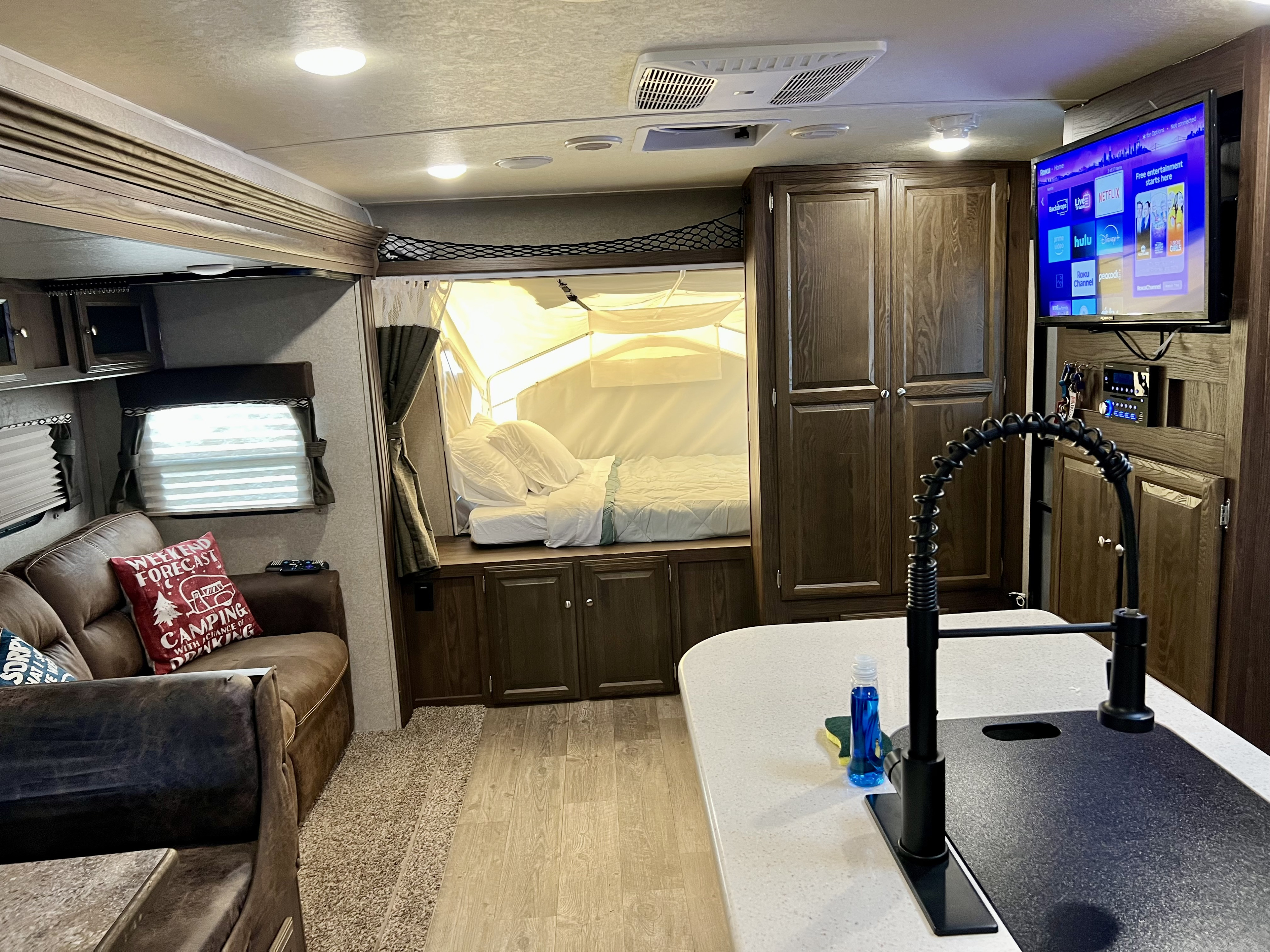 This RV rental interior features a cozy living space with a pop-out bed, kitchen, and TV, perfect for camping adventures.. Forest River Rockwood Roo 2018