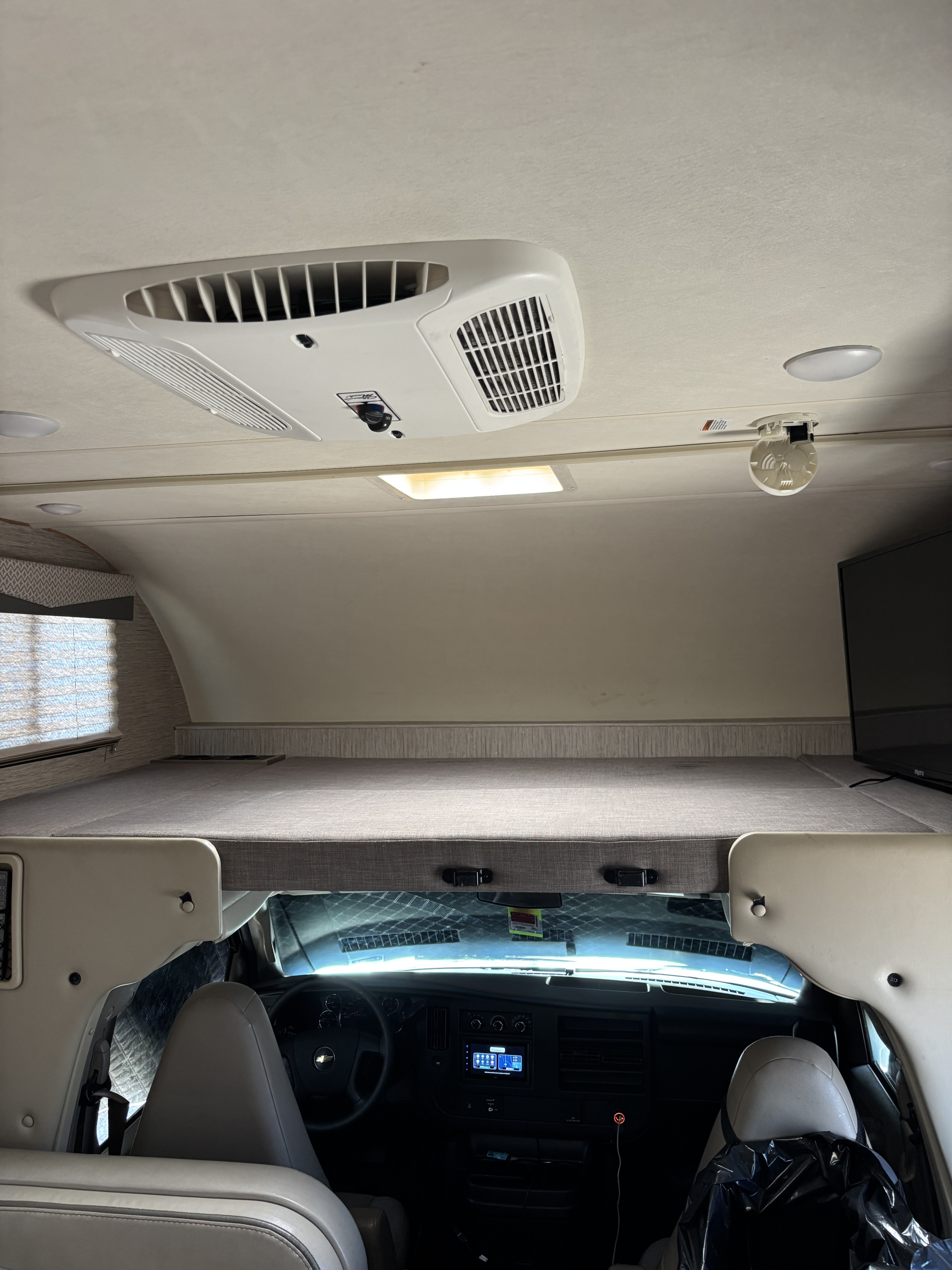 An RV rental interior view, highlighting the overhead bunk, driver's cabin, and ceiling with AC and lights.. Thor Four Winds 2021