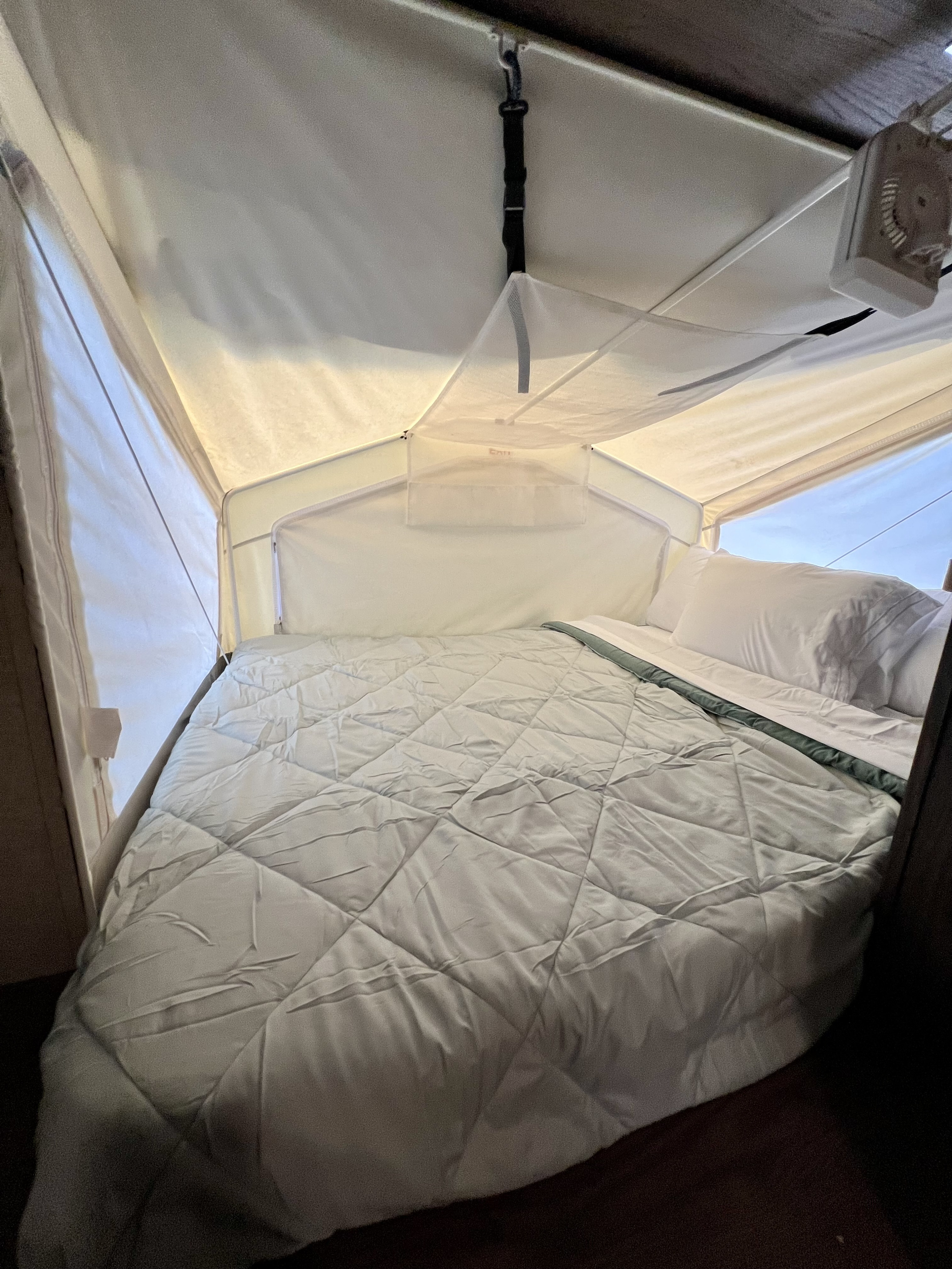 Inside this RV rental pop-up camper, a cozy bed features a grey comforter, white pillows, and soft fabric walls.. Forest River Rockwood Roo 2018