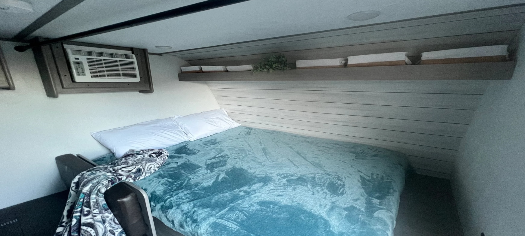 Cozy RV rental bedroom showing a bed with blue blanket, white pillows, wall AC unit, and a decorative shelf.. Dutchmen Coleman Lantern LT 2024